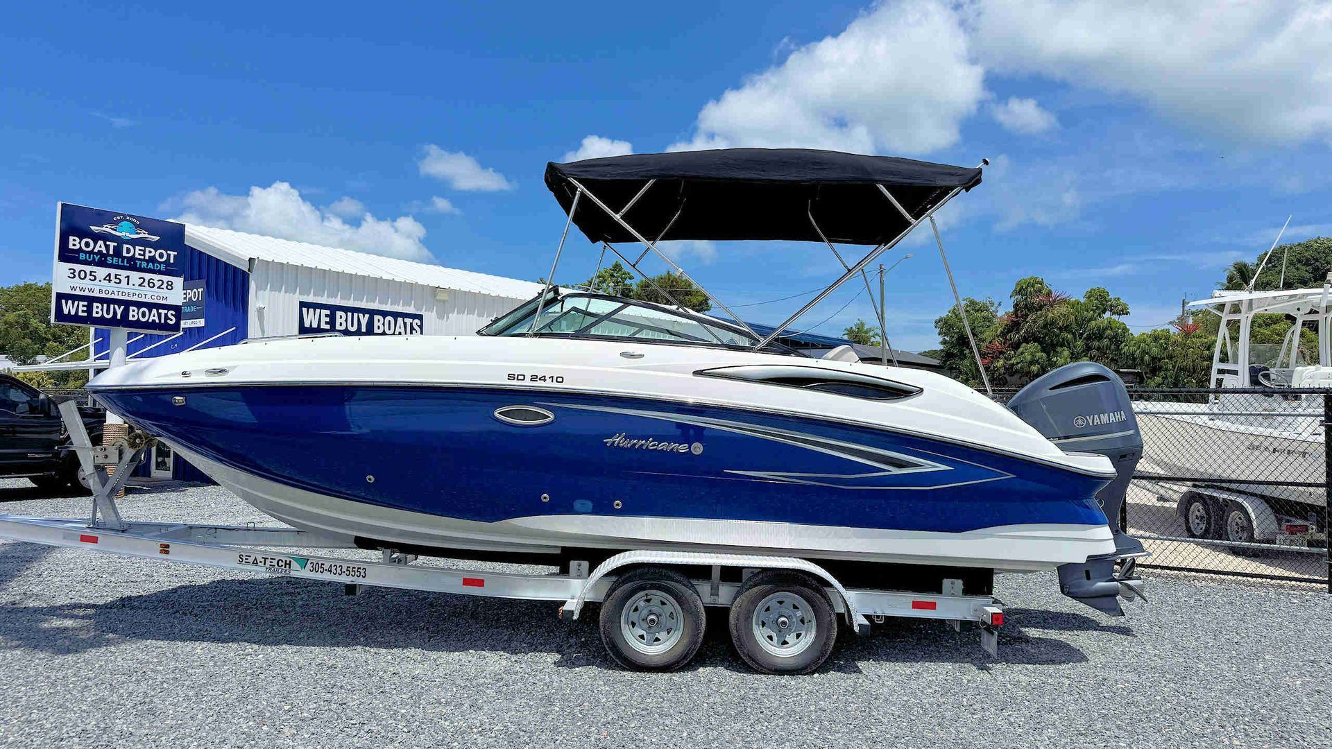 Blue and white speedboat on trailer at a marina, with a black canopy and cloudy blue sky.
