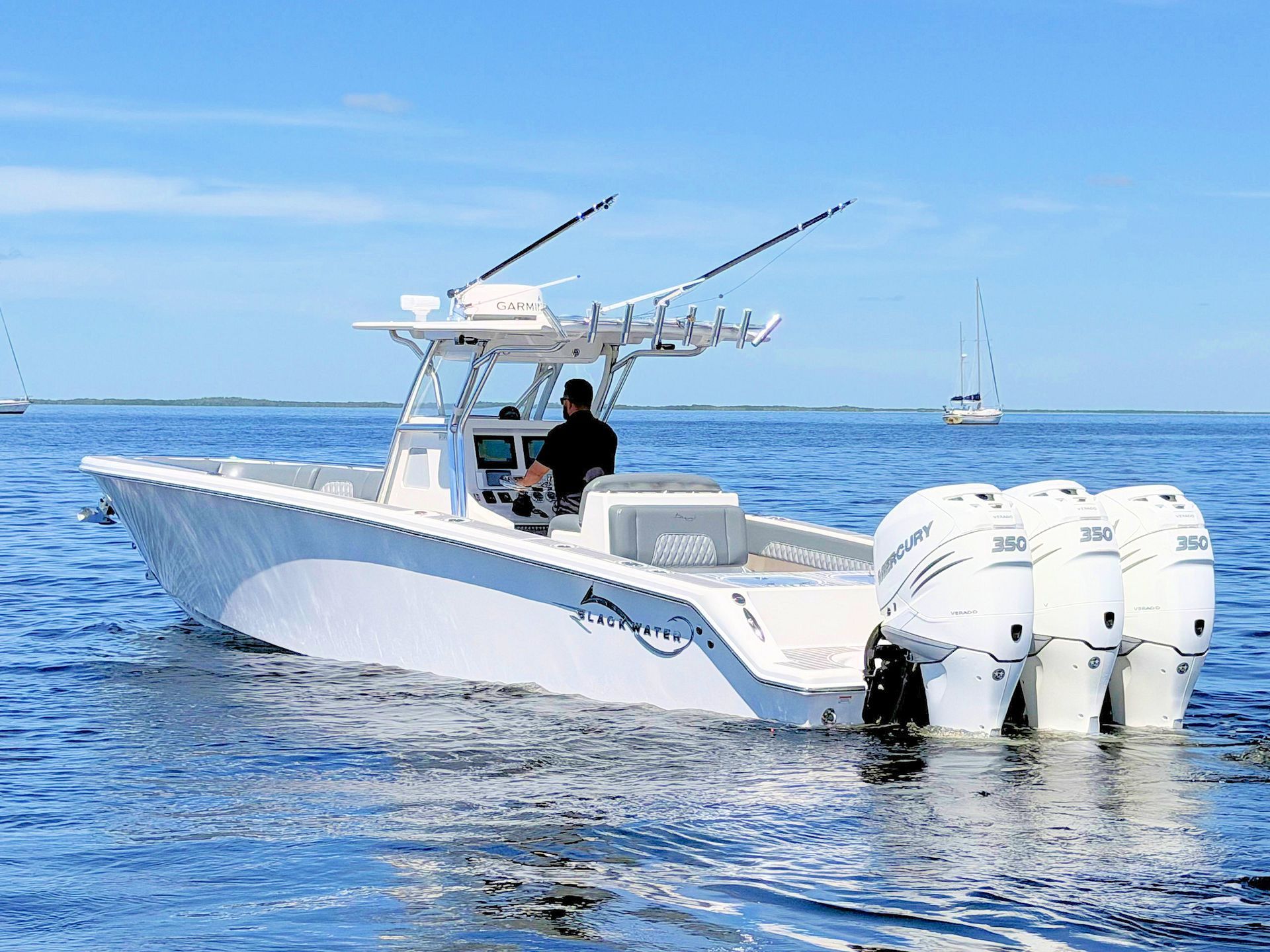 White center-console fishing boat with three outboard motors on blue ocean under a clear sky