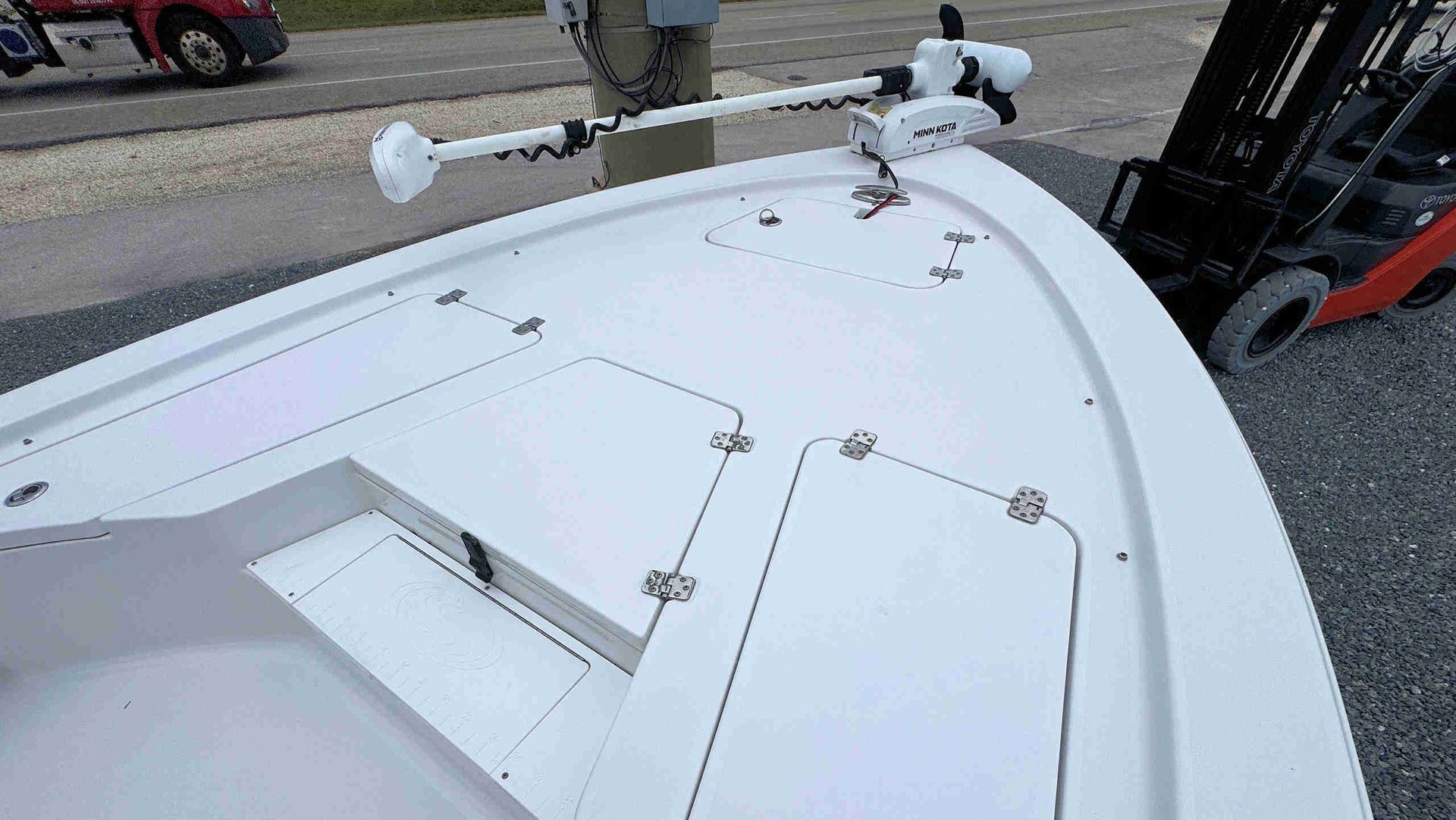White boat deck with hatches and railings, viewed from above beside a forklift in a parking lot.