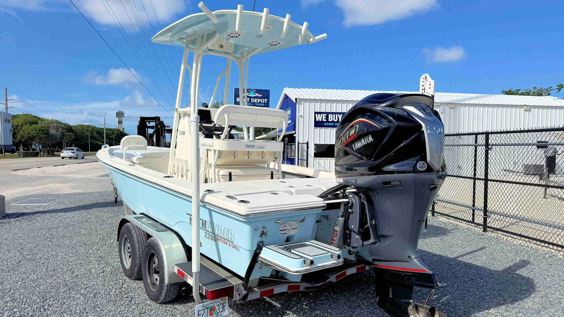 Small white center-console fishing boat on a trailer, parked on gravel with an outboard motor and T-top.