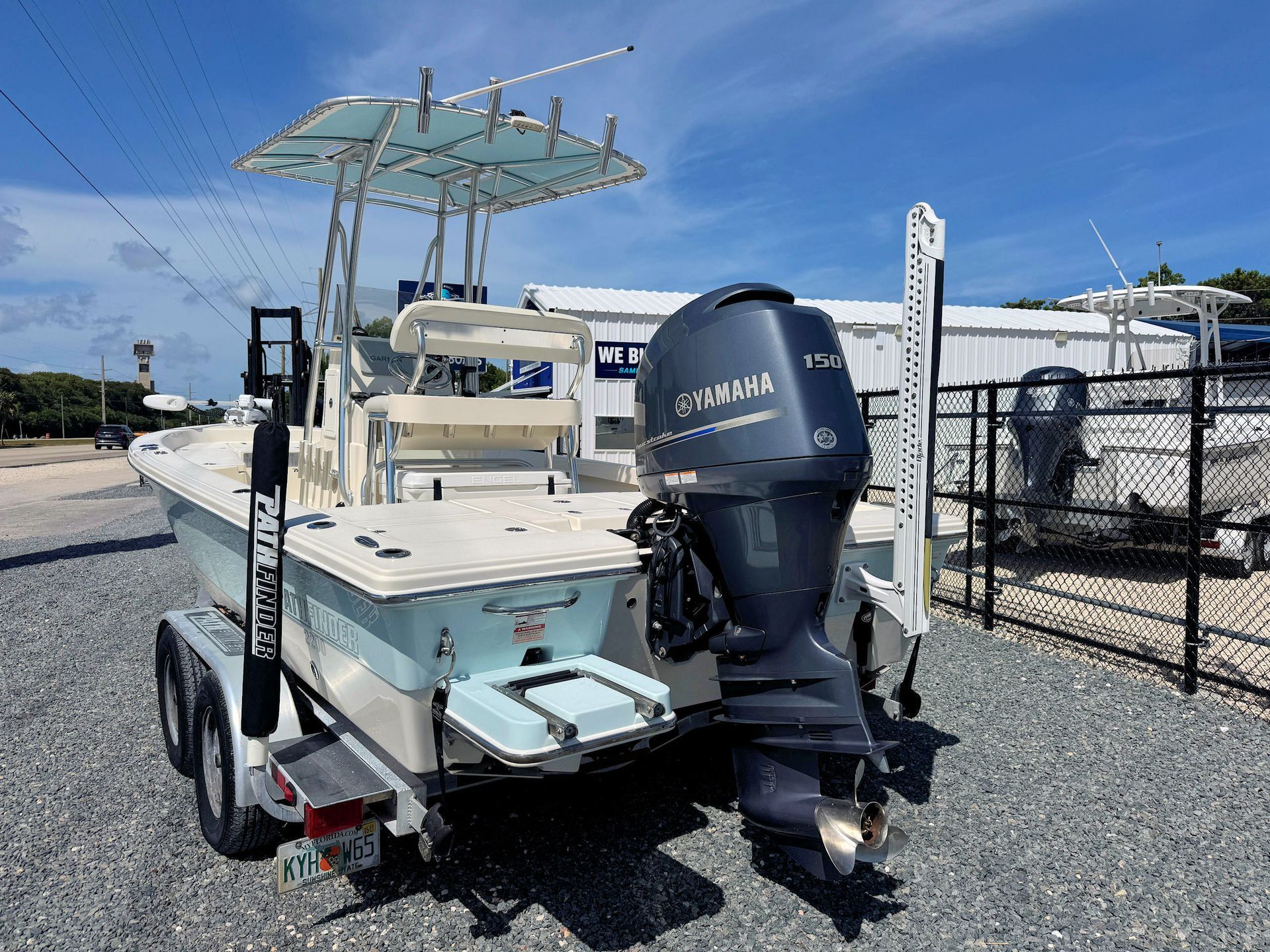 Small white fishing boat with grey outboard motor parked on a gravel lot under a clear sky.