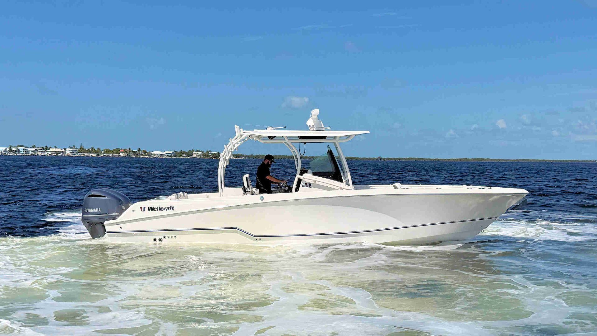 White center-console speeding across blue water with two people aboard under a canopy