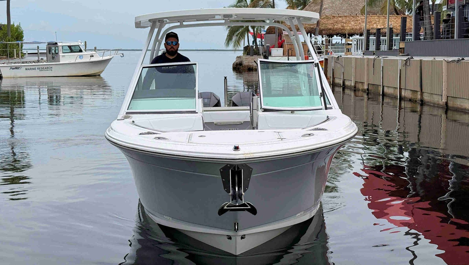 White motorboat docked at a marina, facing forward on calm water.