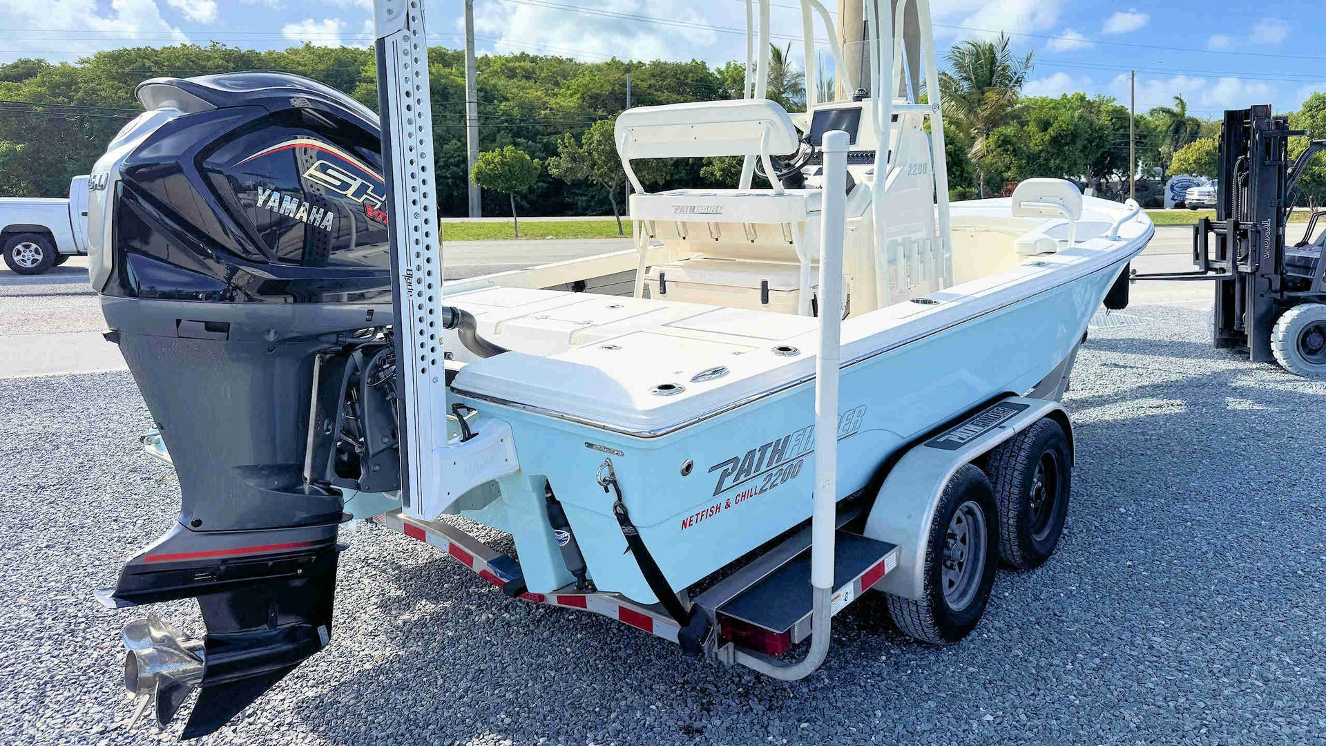 White center-console fishing boat on a trailer, rear view, with outboard motor on a gravel lot.