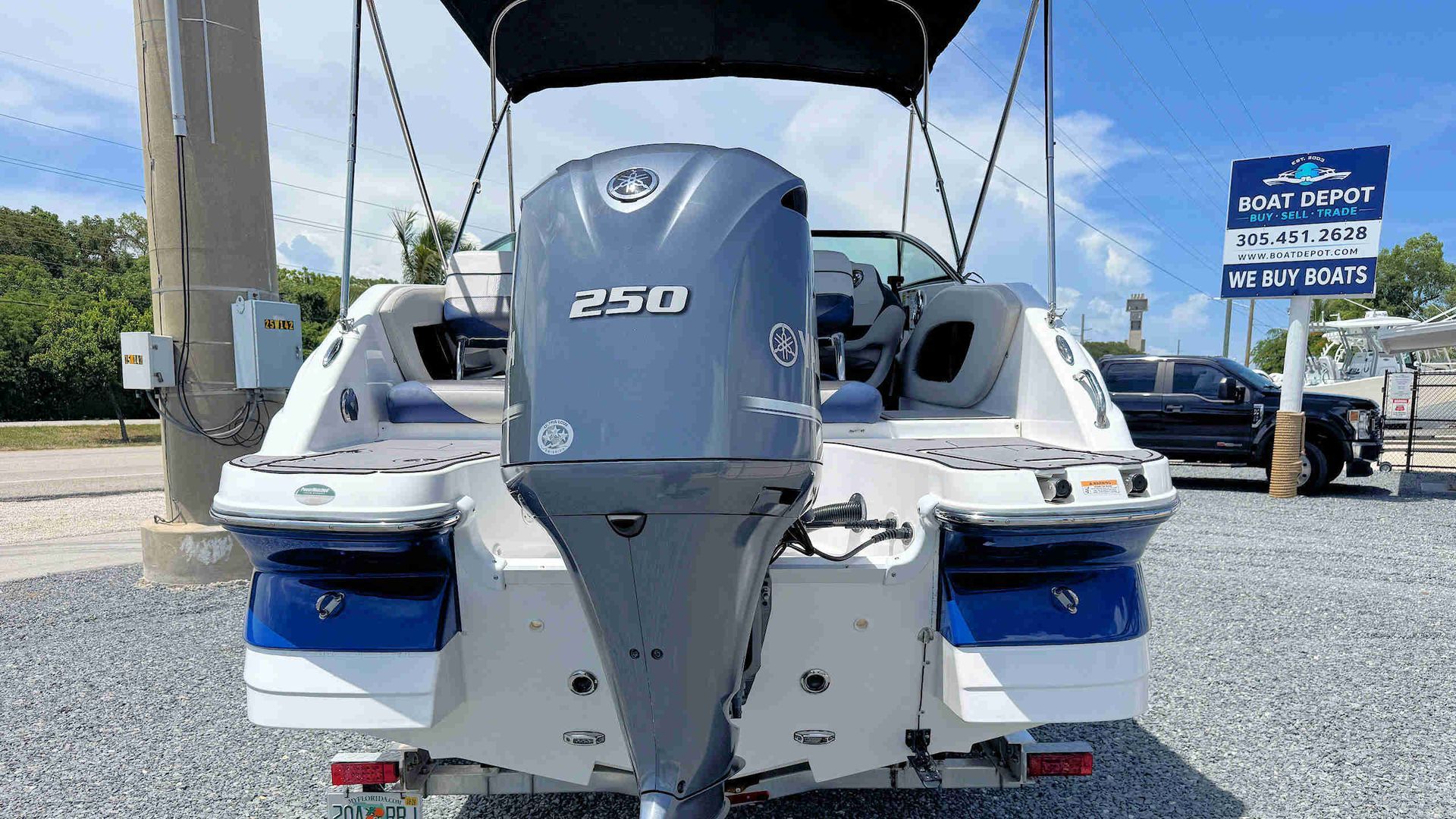 Rear view of a white boat with a Yamaha 250 HP outboard motor at a gravel boat lot.