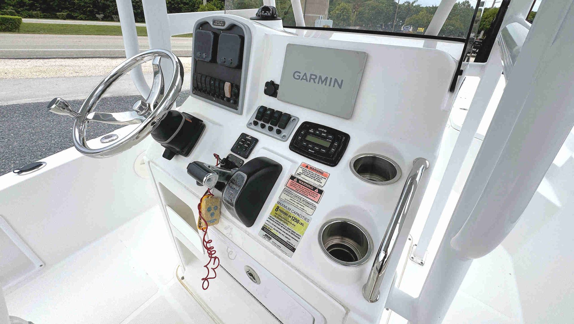 Boat helm with steering wheel, Garmin display, switches, and cup holders on a white console