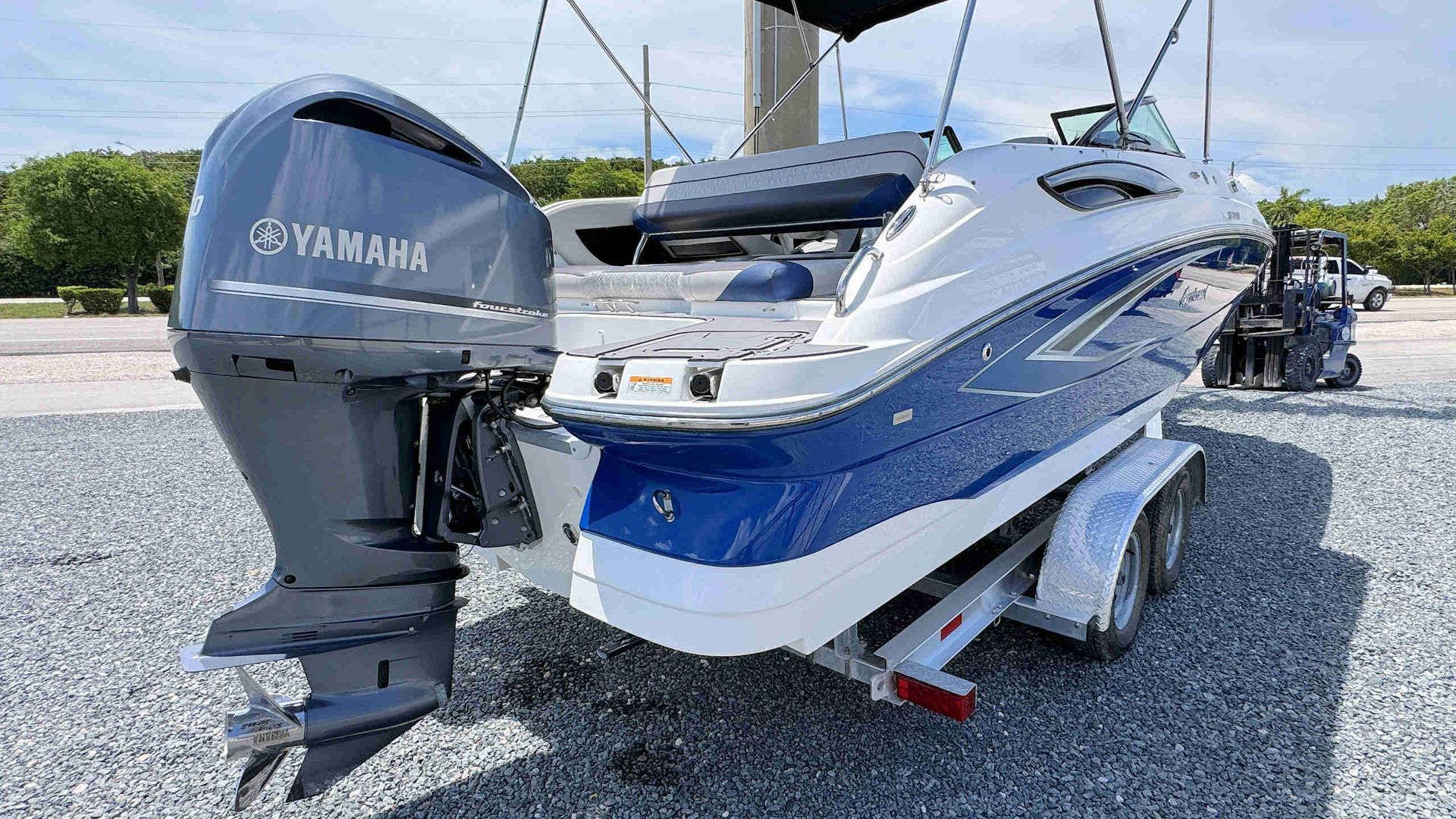 Blue-and-white speedboat on a trailer in a gravel lot, viewed from the stern.