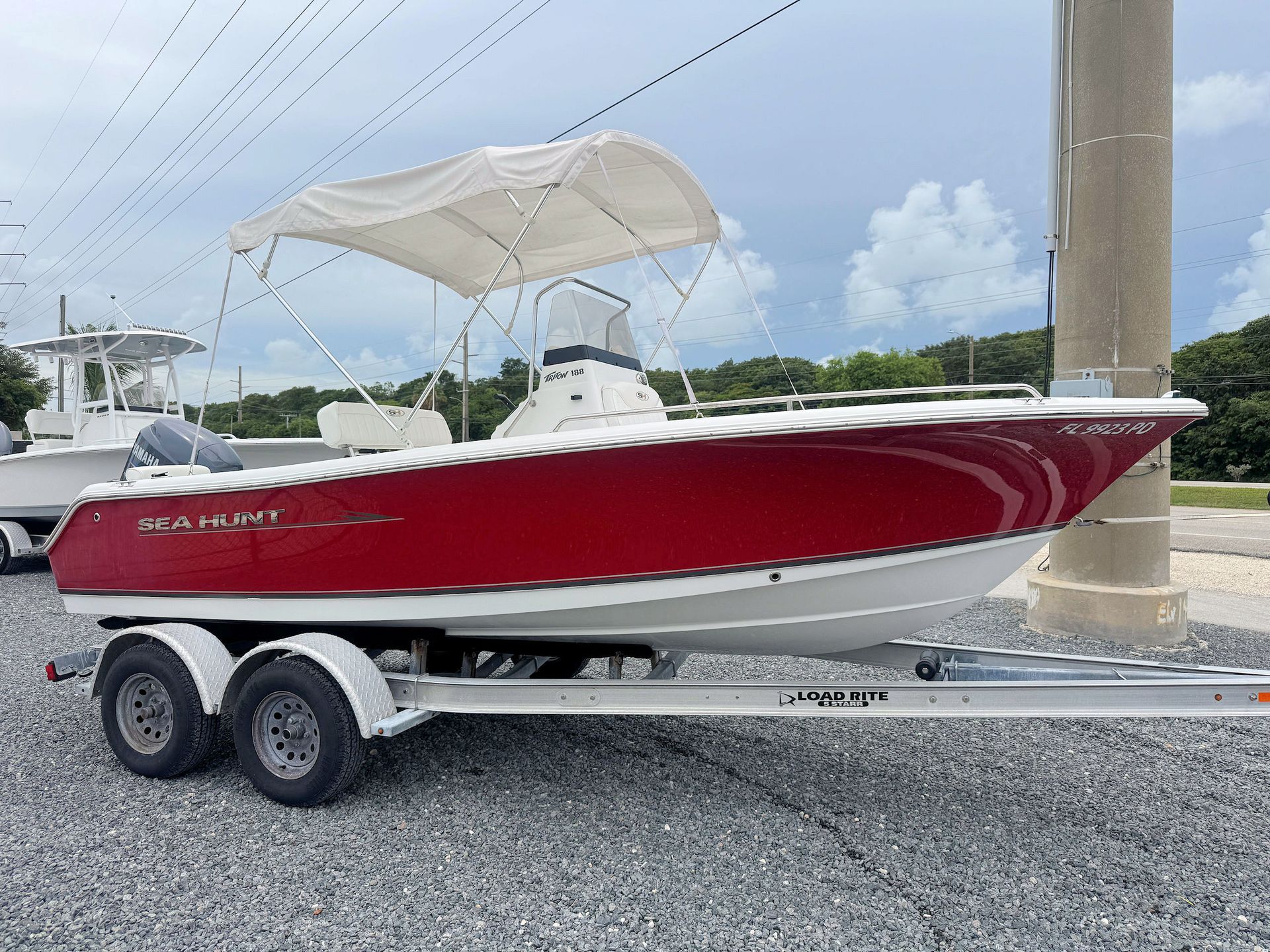 Red boat on a trailer with a white bimini top, parked on a marina lot under a cloudy sky.