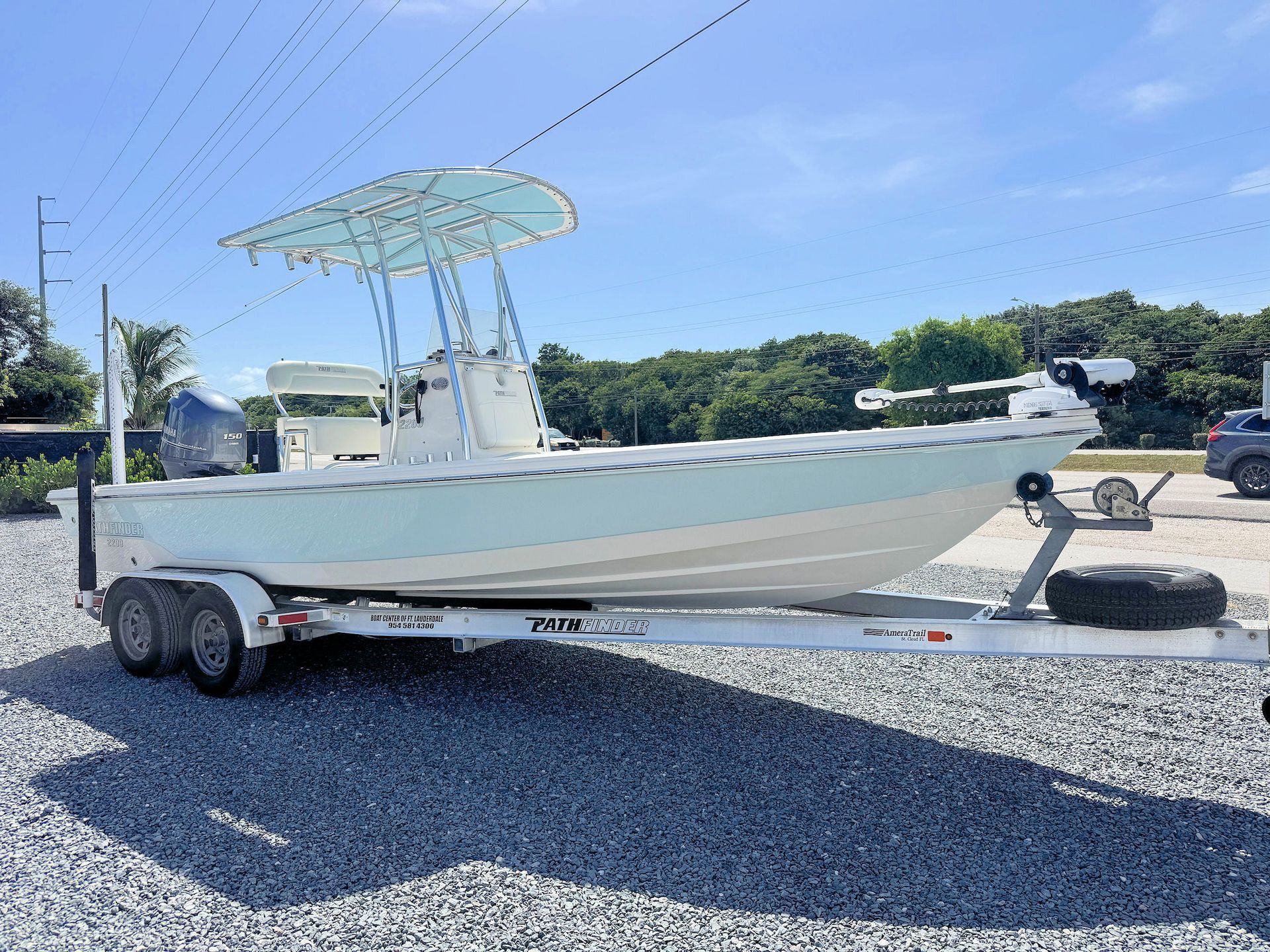 White center-console boat on a trailer in a gravel lot under a blue sky