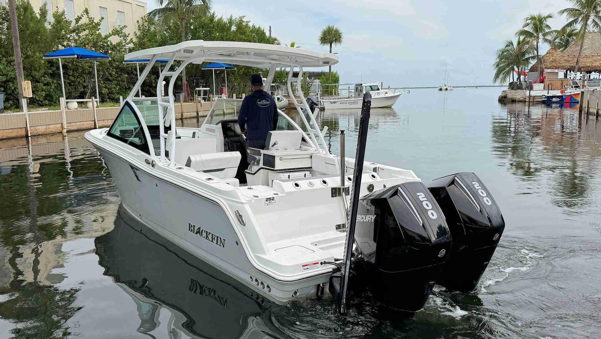 White motorboat with twin outboard engines docked on calm water, with a person standing aboard