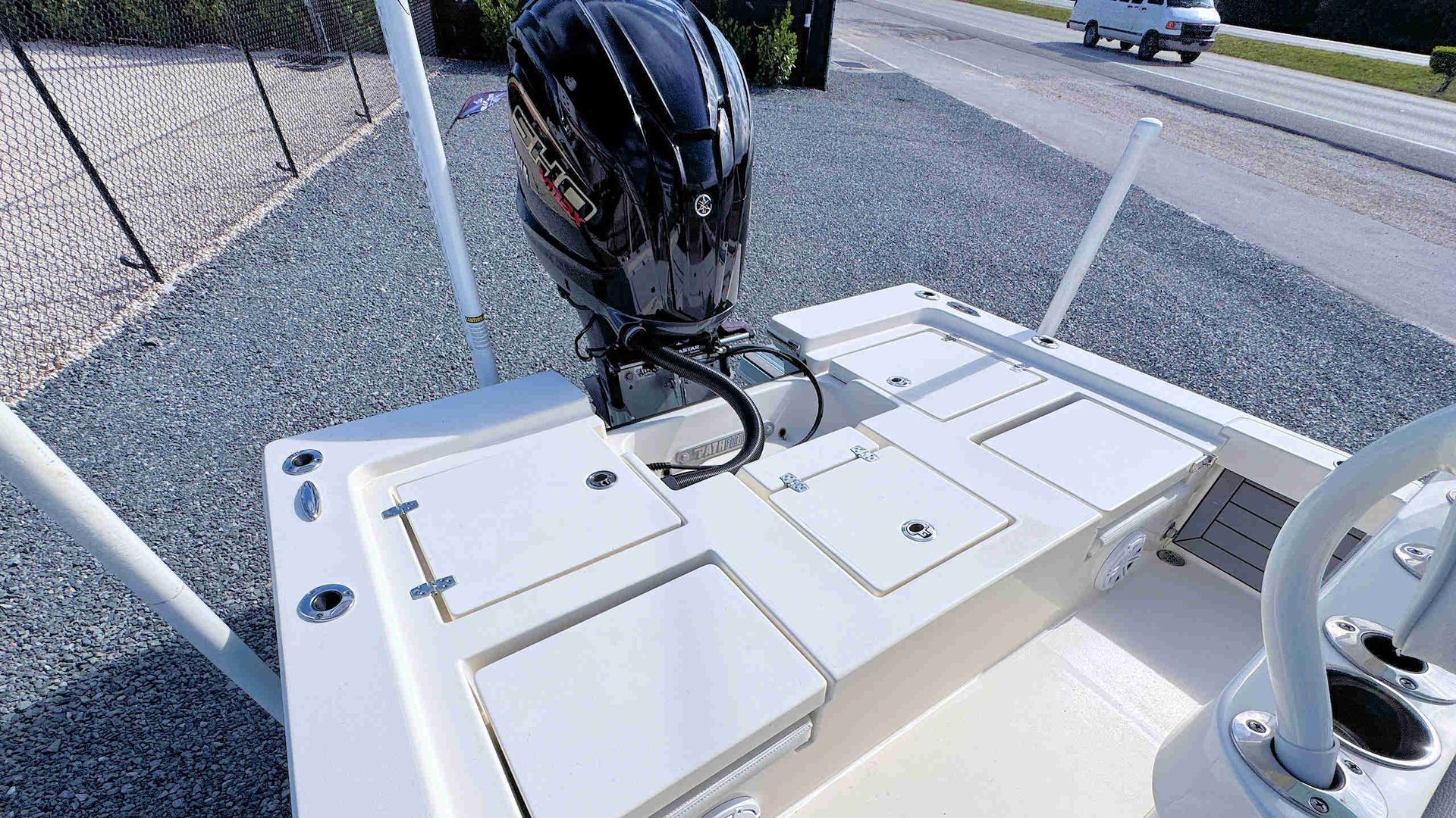 White boat deck with an outboard motor, storage hatches, and a roadside parking area nearby