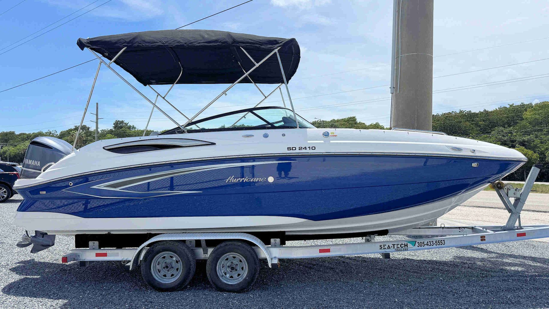 Blue and white speedboat on a trailer with a black canopy, parked outdoors under a clear sky