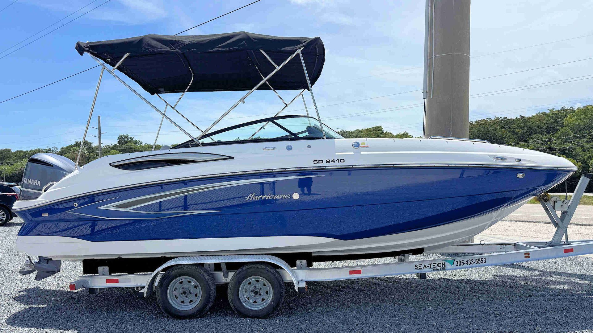 Blue and white speedboat on a trailer with a canopy, parked outdoors under a clear sky
