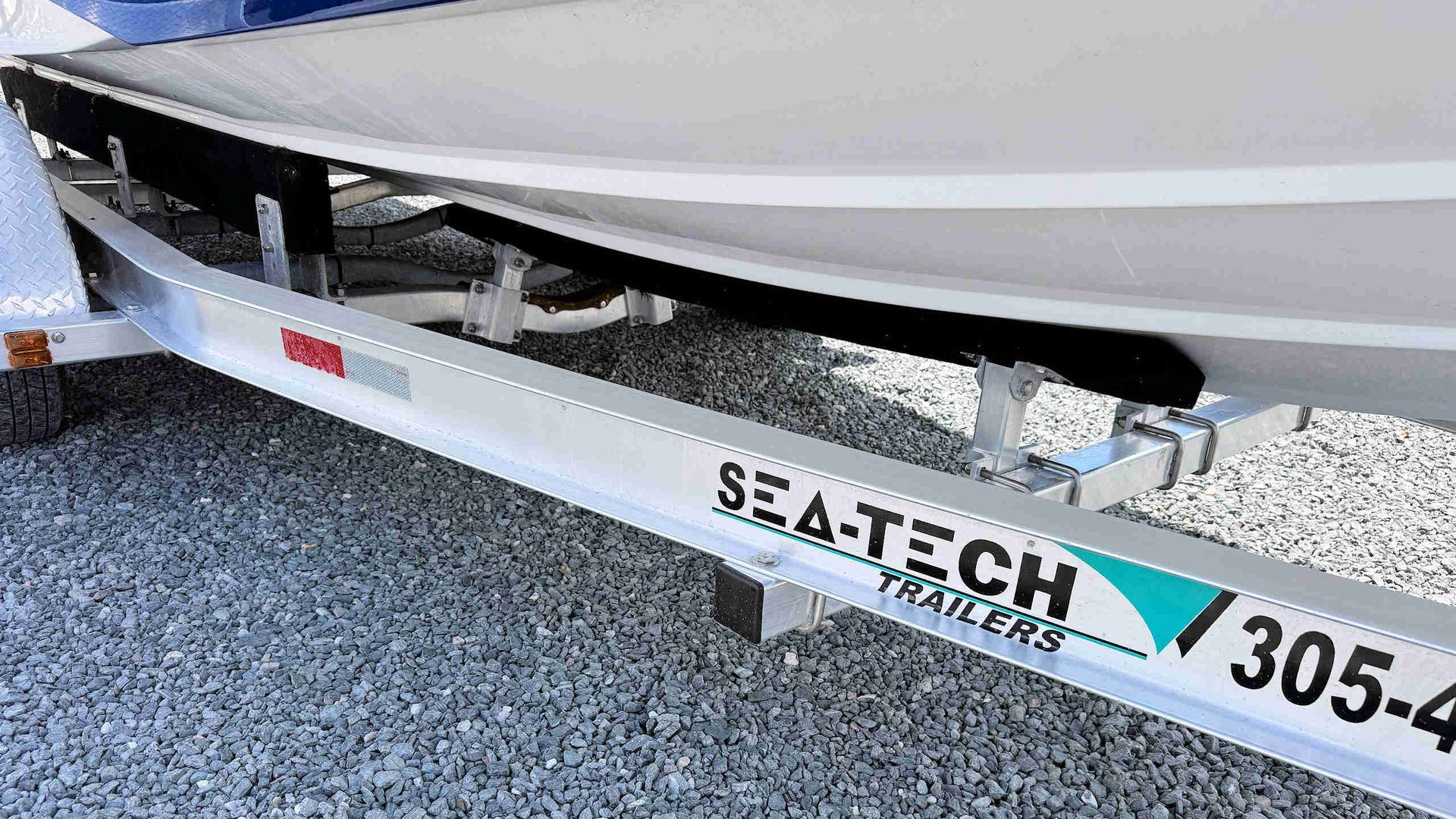 Boat on a trailer with Seatech logo and registration number, parked on gravel.