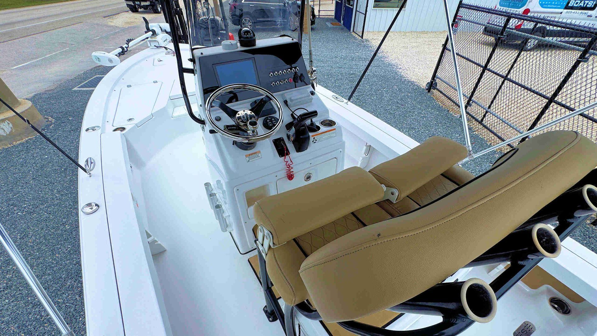 Tan-and-white boat deck with helm, tan seats, and fishing rod holders, docked beside a marina walkway.