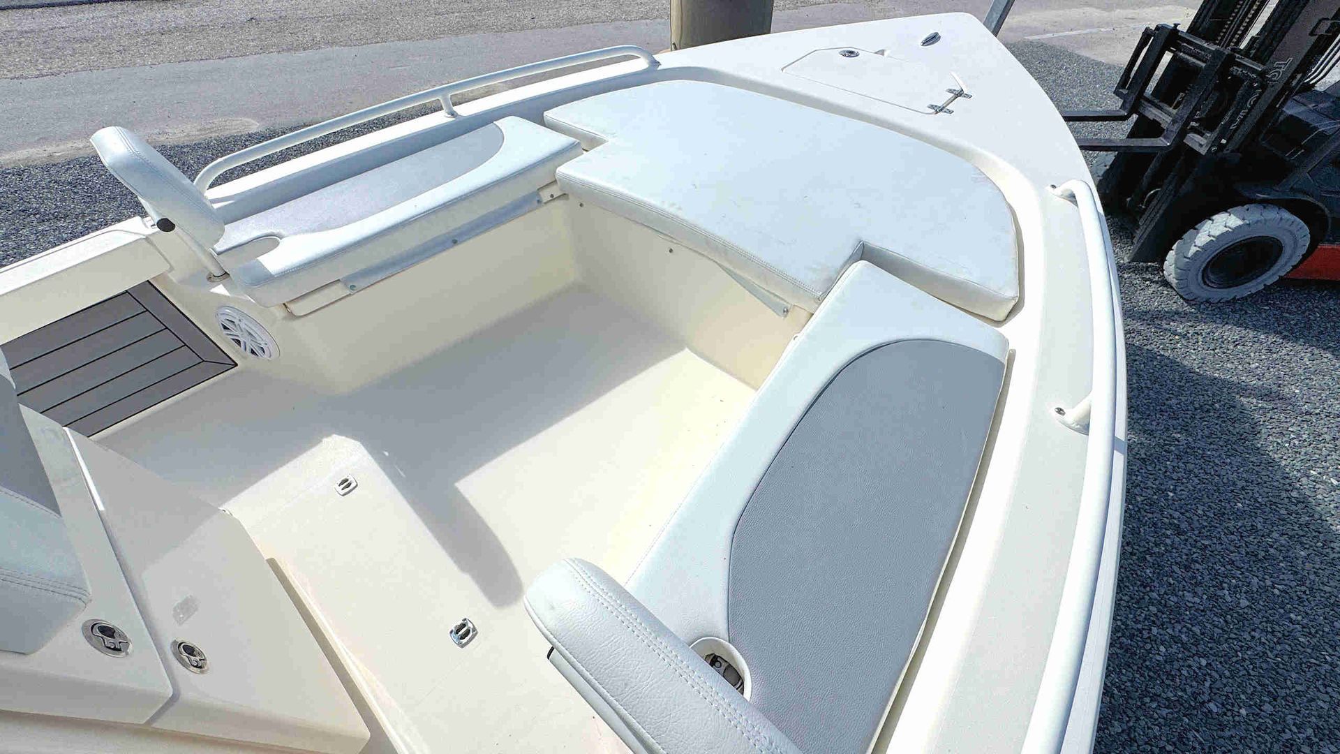 White boat cockpit with bench seats and steering wheel on a gravel lot
