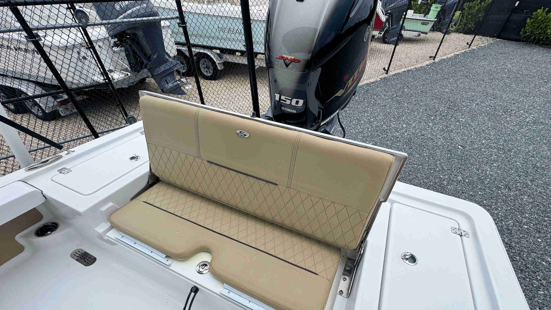 Beige cushioned boat bench seat on a white deck, with a black outboard motor behind it.