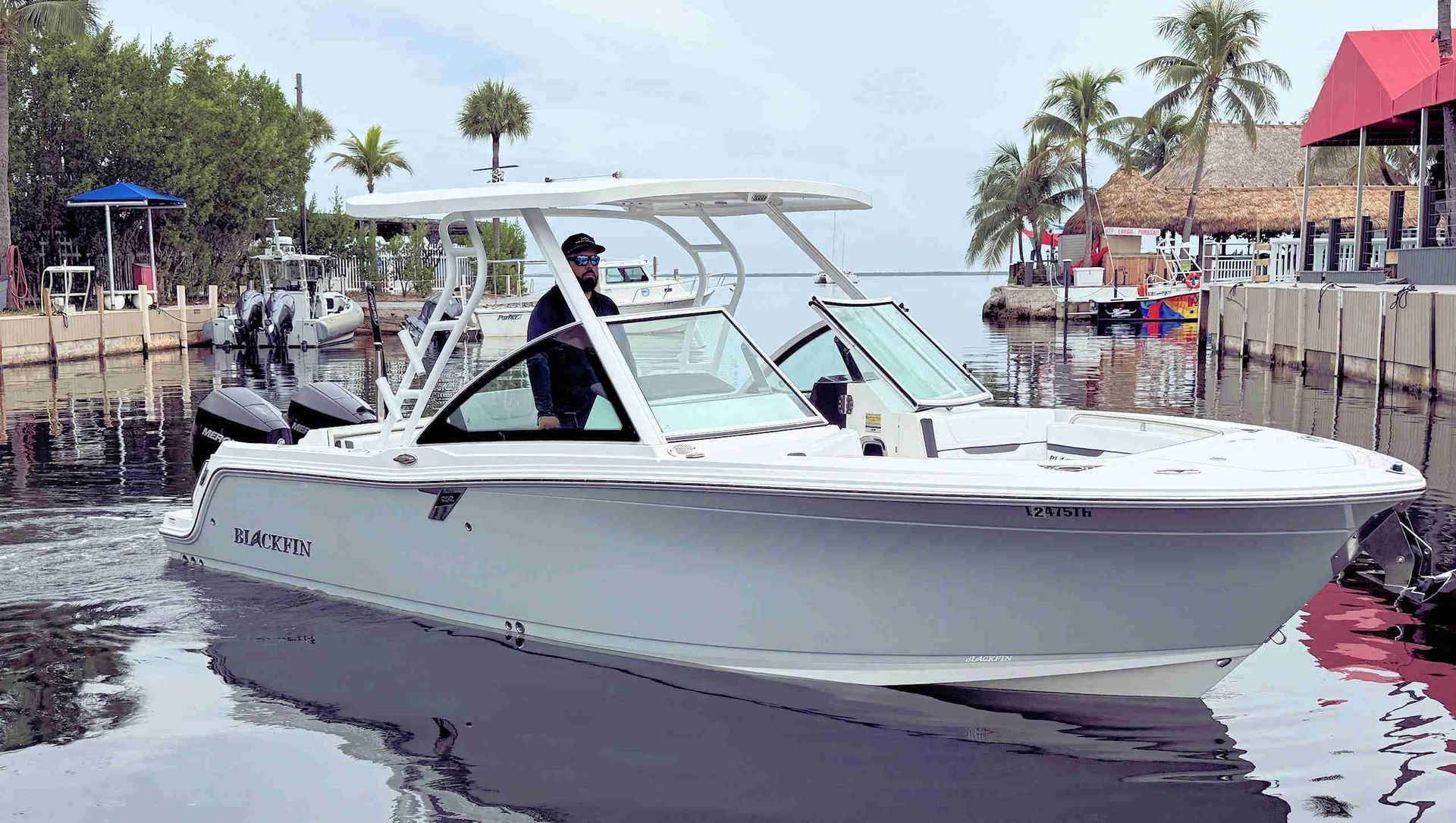 White motorboat cruising in a marina with palm trees and docked boats in the background