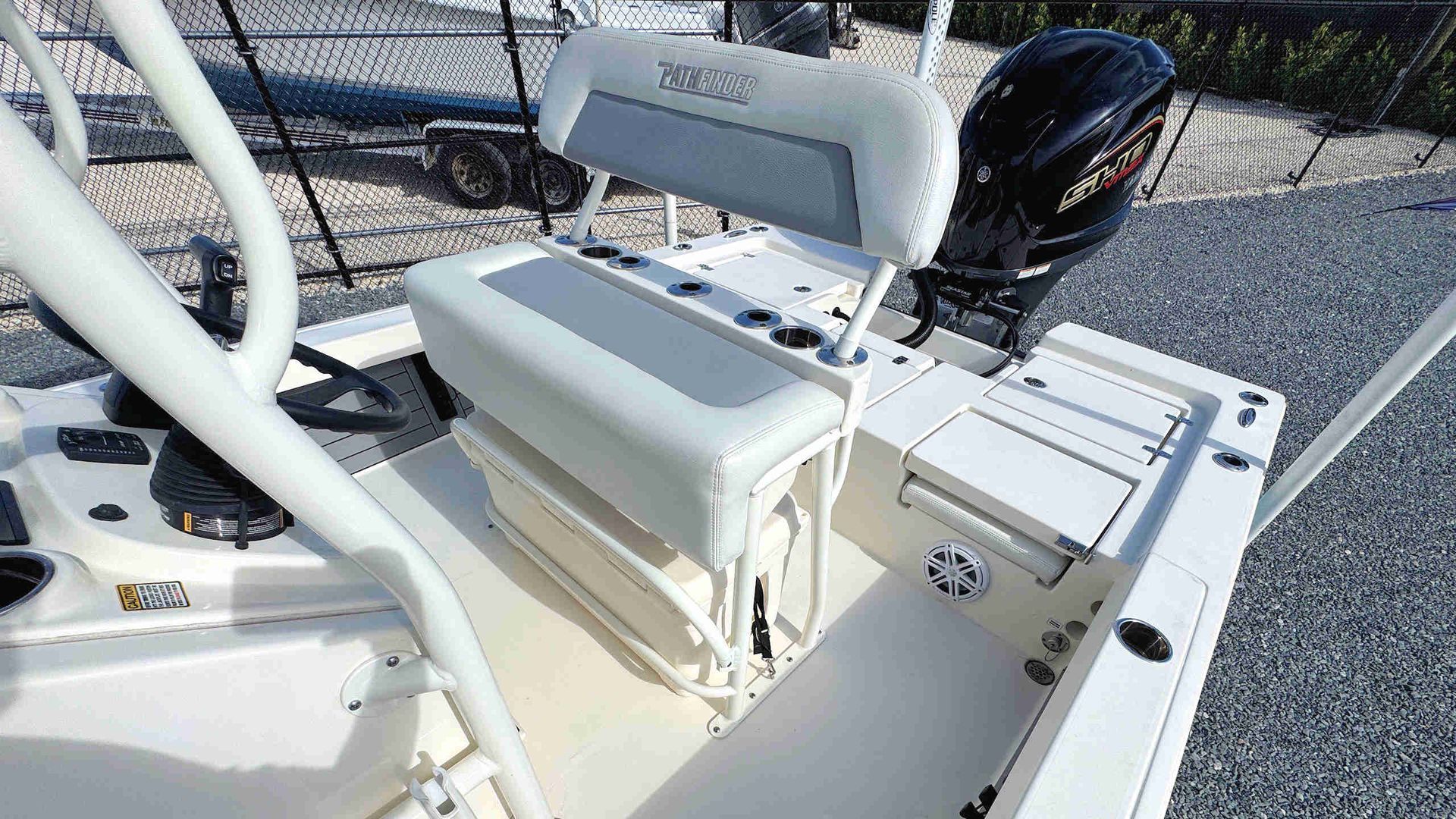 White boat cockpit with padded bench seat, steering console, and black outboard motor on a sunny day