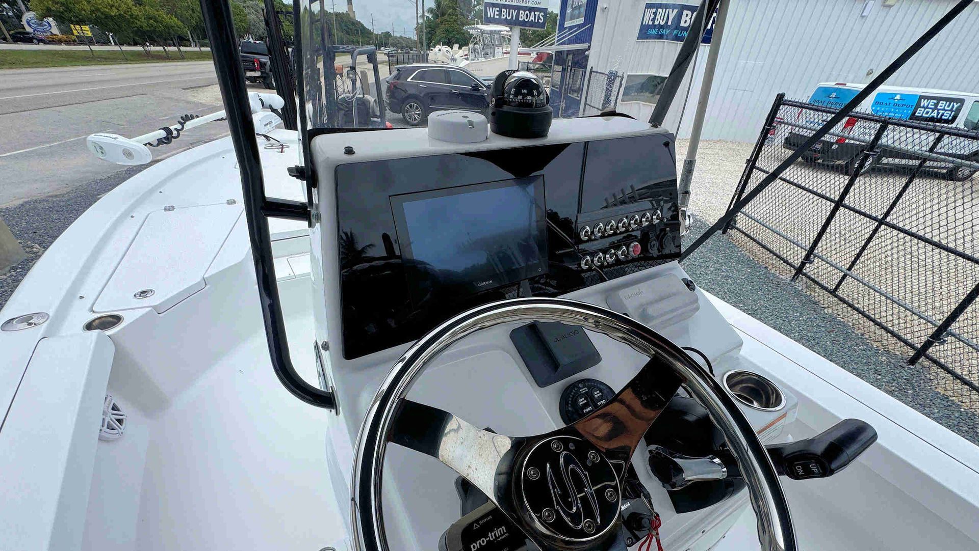 Boat helm with steering wheel and navigation screen on a white deck, dock and parked vehicles in background
