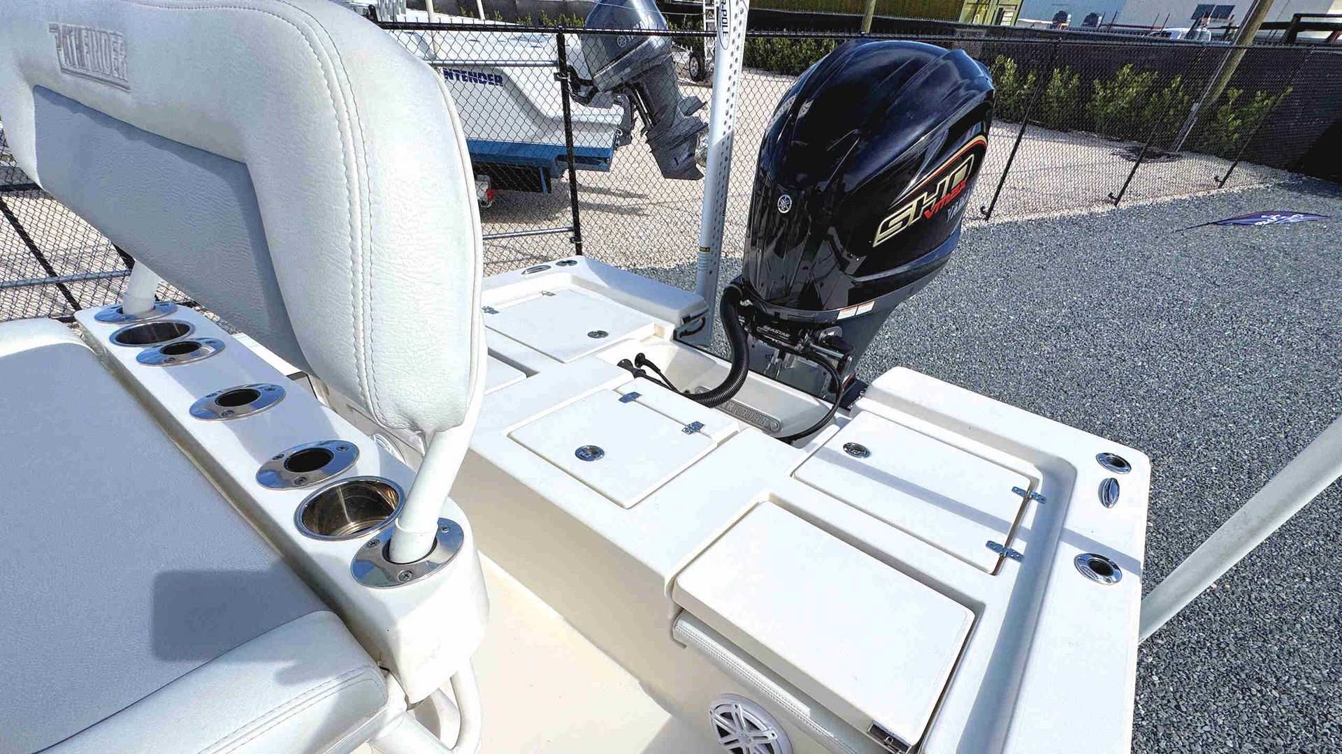 Boat stern with white seats, fishing rod holders, and a black outboard motor on a trailer.
