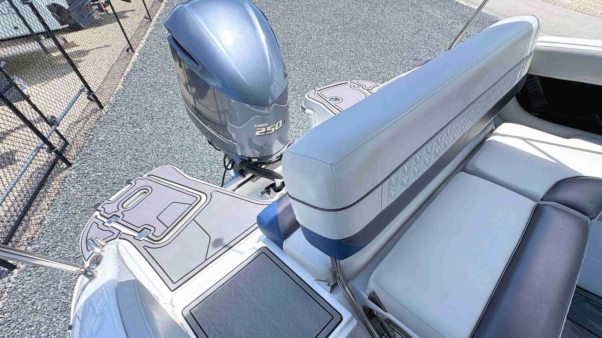 Boat deck with white seating, gray flooring, and a metallic outboard motor by a chain-link fence.