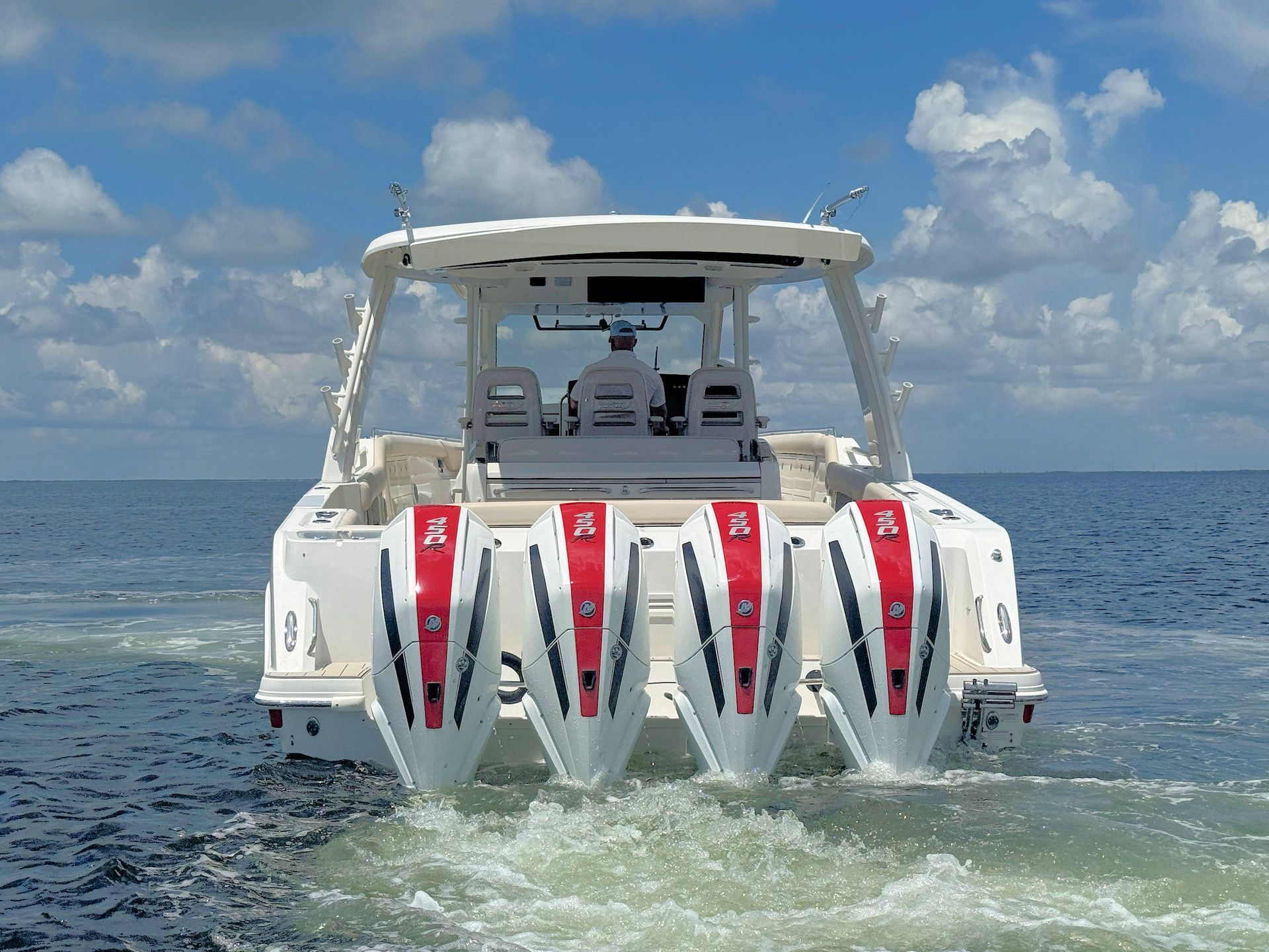 White offshore fishing boat viewed from stern, on open water under a cloudy sky.