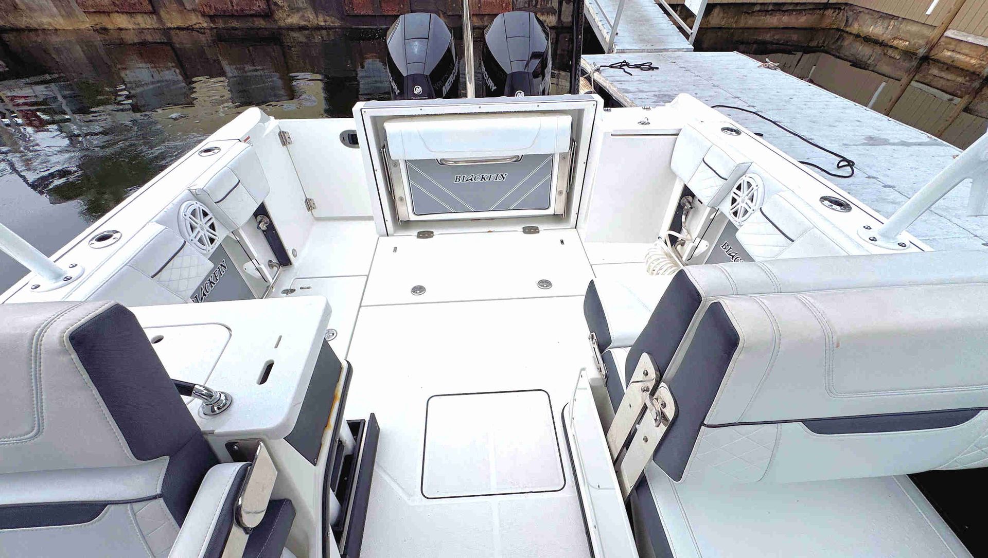 White boat cockpit with built-in seats and central deck hatch, viewed from above in daylight