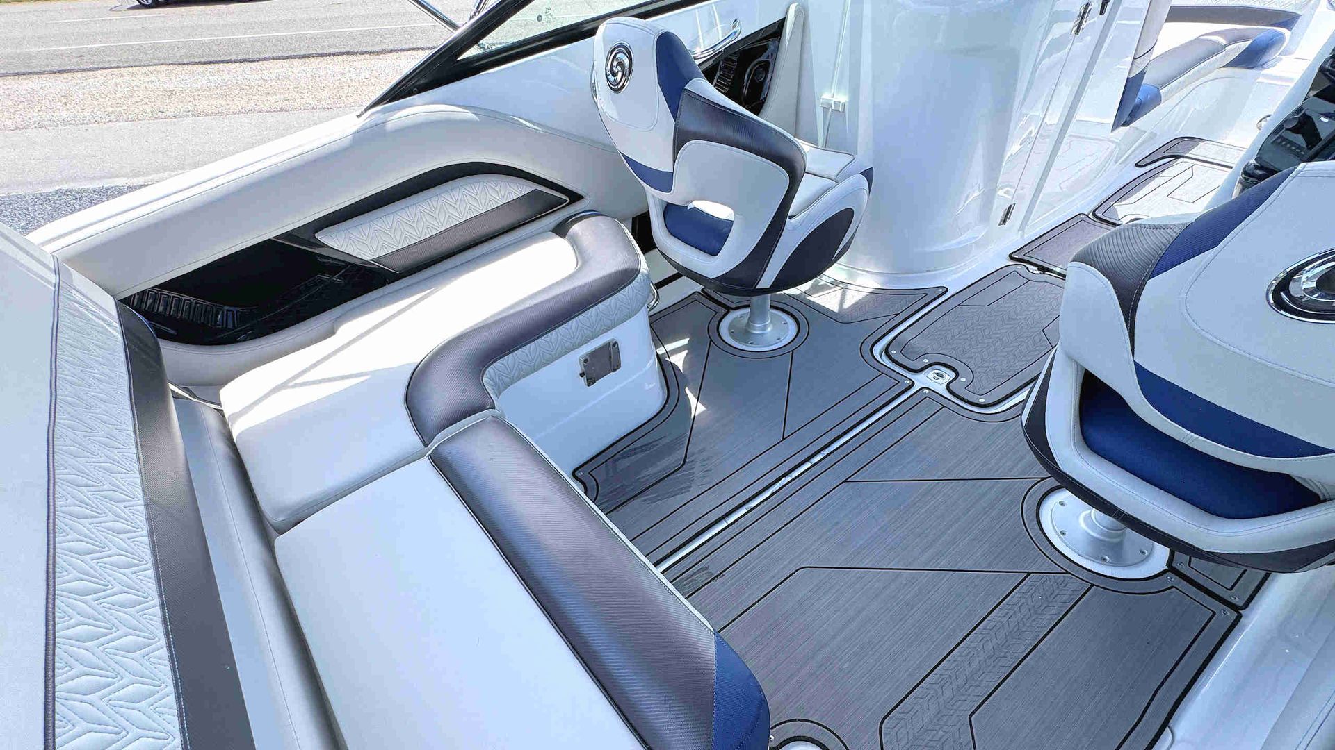 Aft deck of  speedboat with white and blue seats, gray flooring, and a steering wheel near the helm.