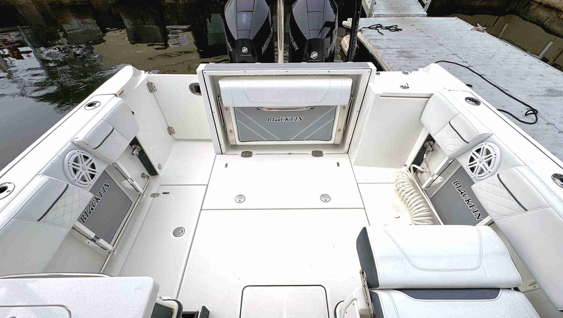 White boat cockpit with cushioned seating around a central hatch, viewed from above on a docked vessel