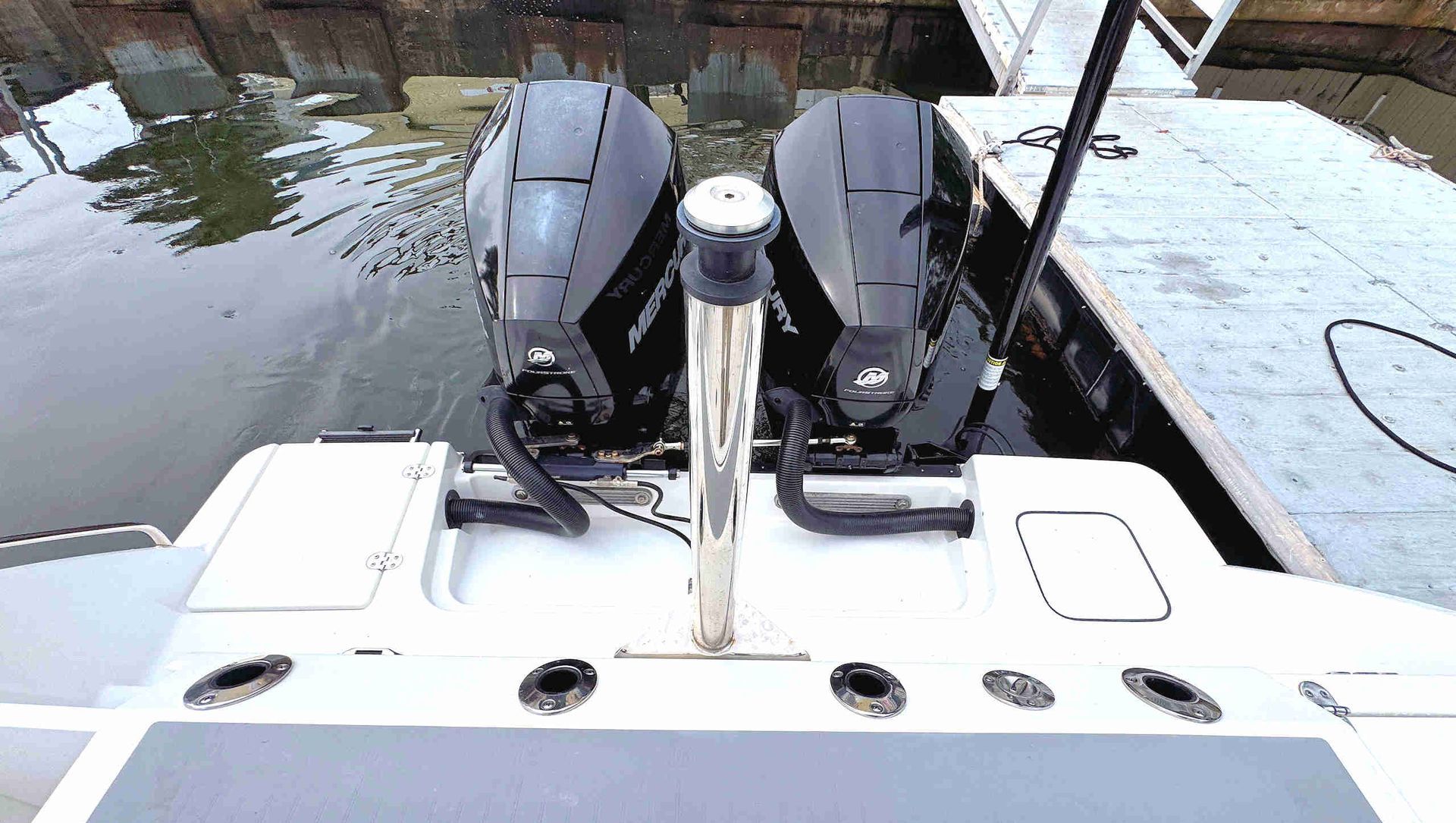 Boat stern with twin outboard motors and white deck at a dockside canal.