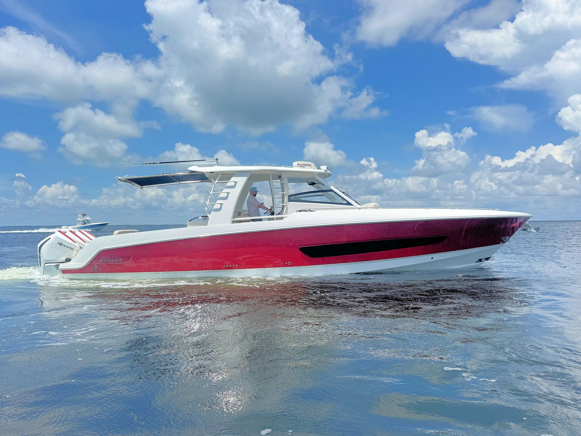 White and red center-console boat for sale  cruising on calm blue water under a partly cloudy sky