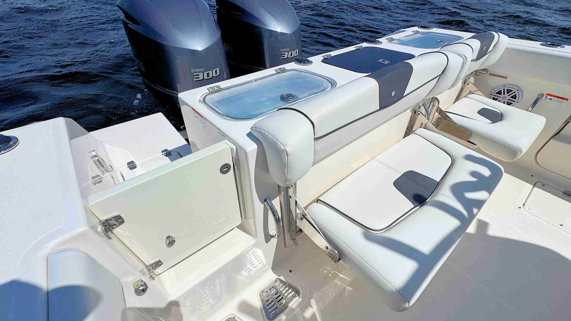 Boat deck with white seating and storage benches beside dark blue hulls on a sunny day
