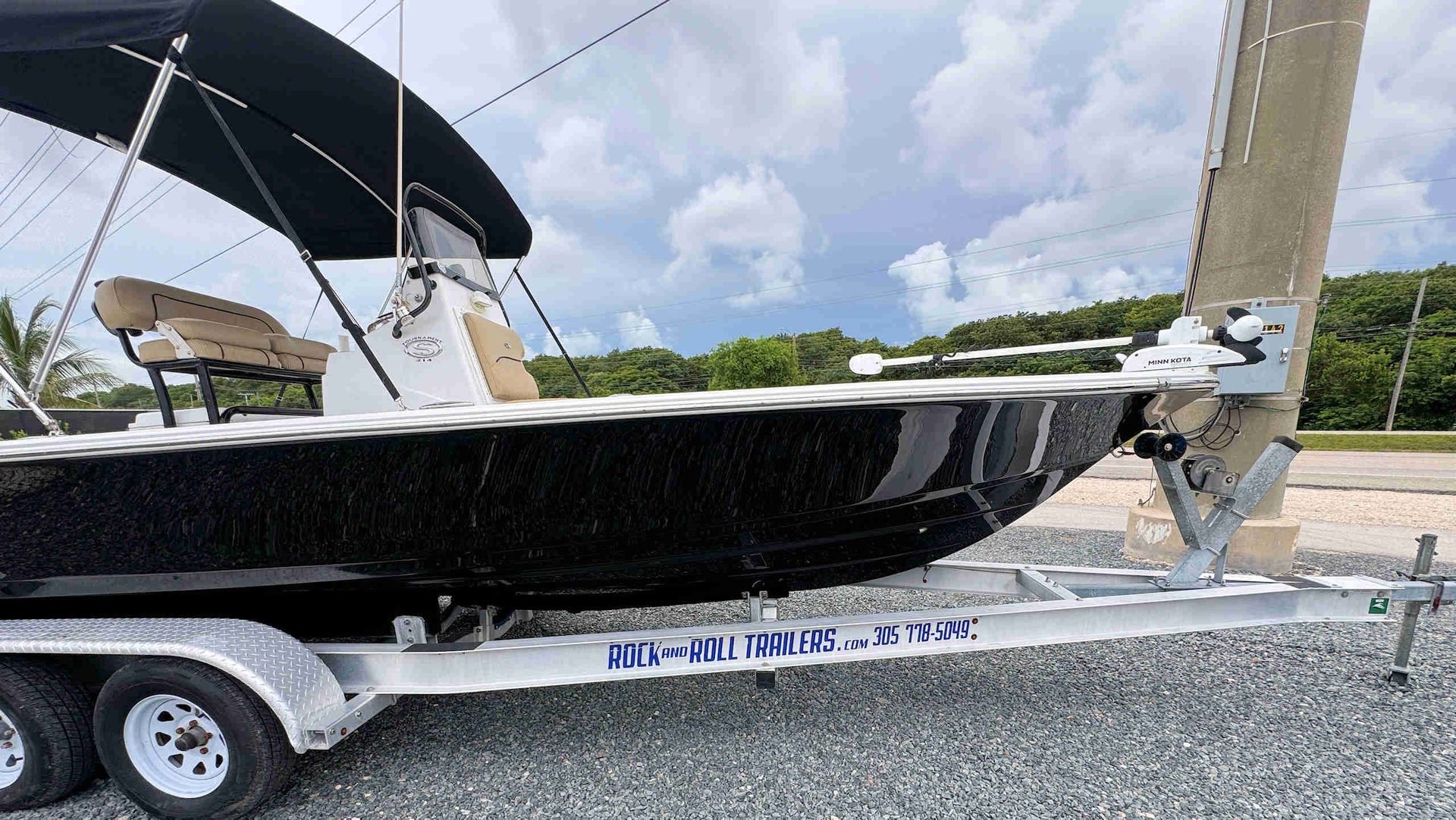Black center console boat on a trailer beside a dock under a cloudy sky