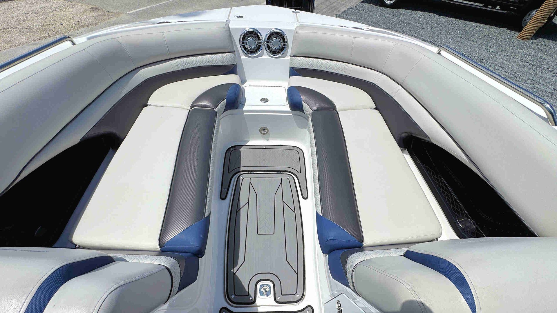 Boat foredeck with white and blue cushioned seats and central console on calm water
