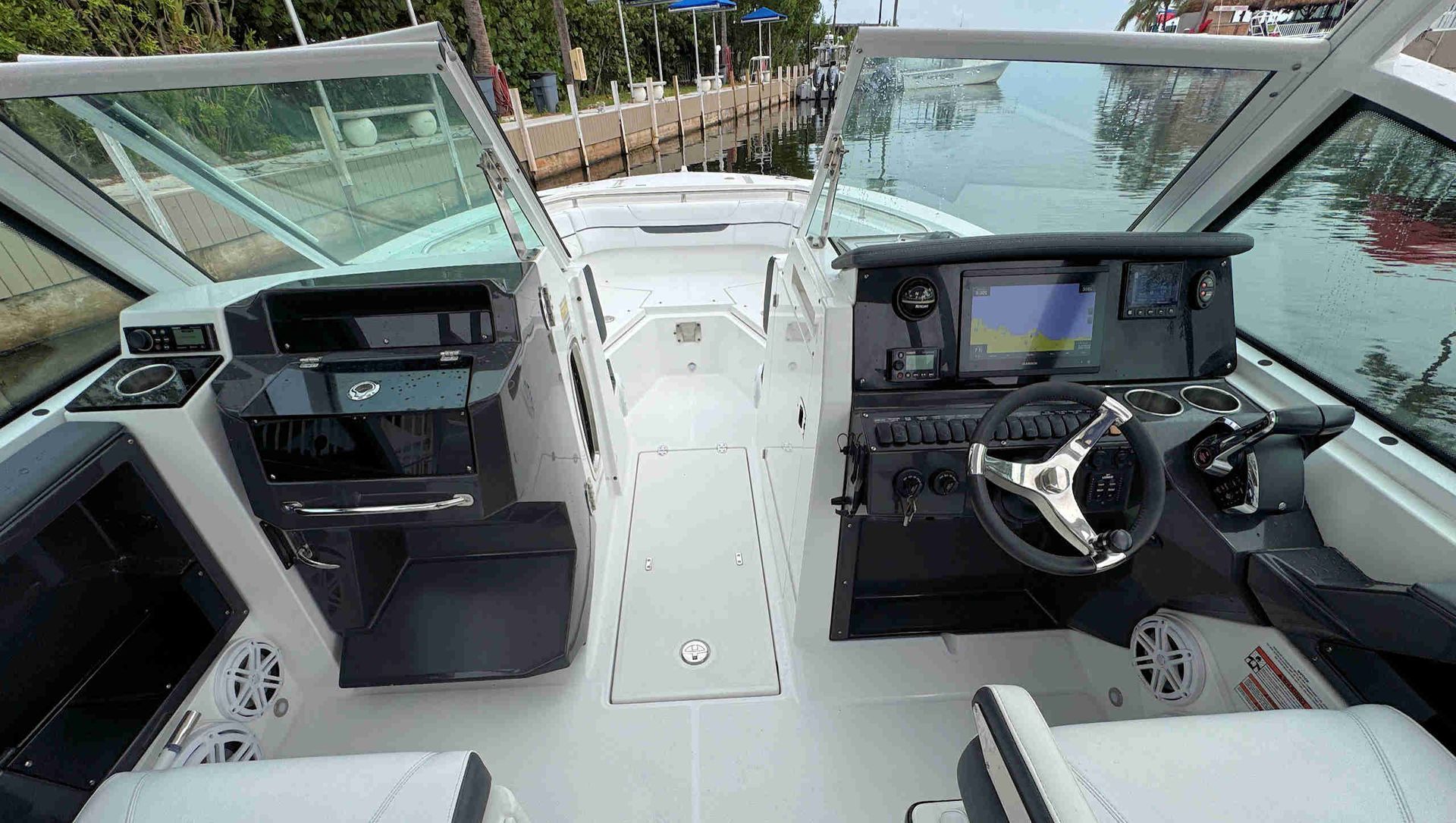 Boat cockpit with twin consoles, white deck, and marina water visible ahead