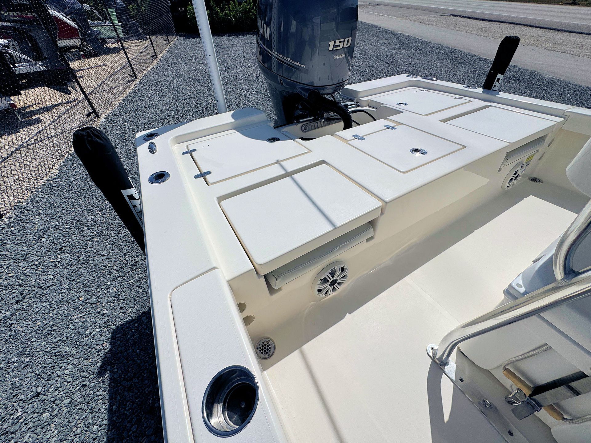 Cream-colored boat deck with hatches, cup holders, and a grey outboard motor on gravel.