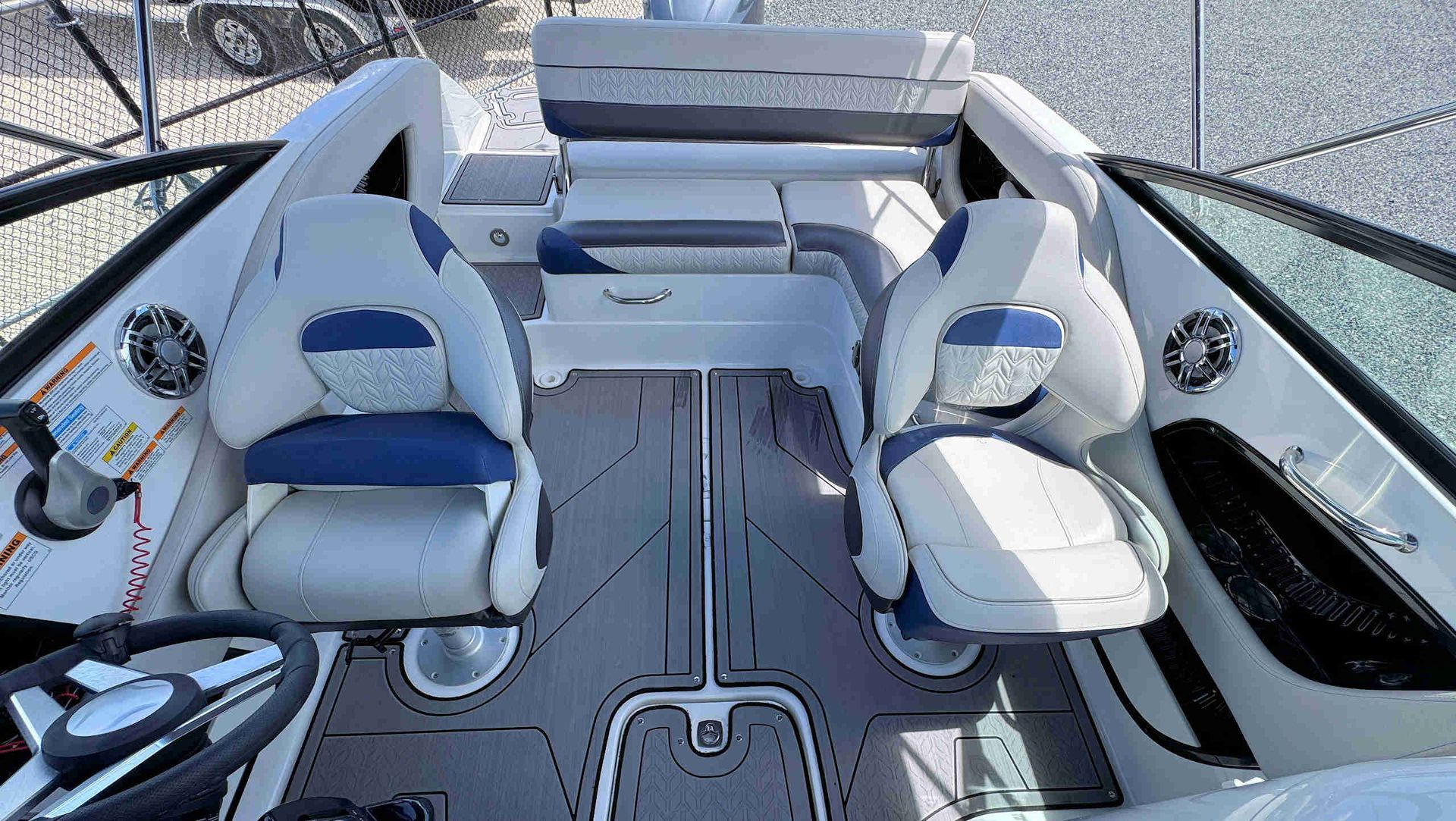 Boat cockpit with two white-and-blue seats, a central walkway, and a windshield view over the water