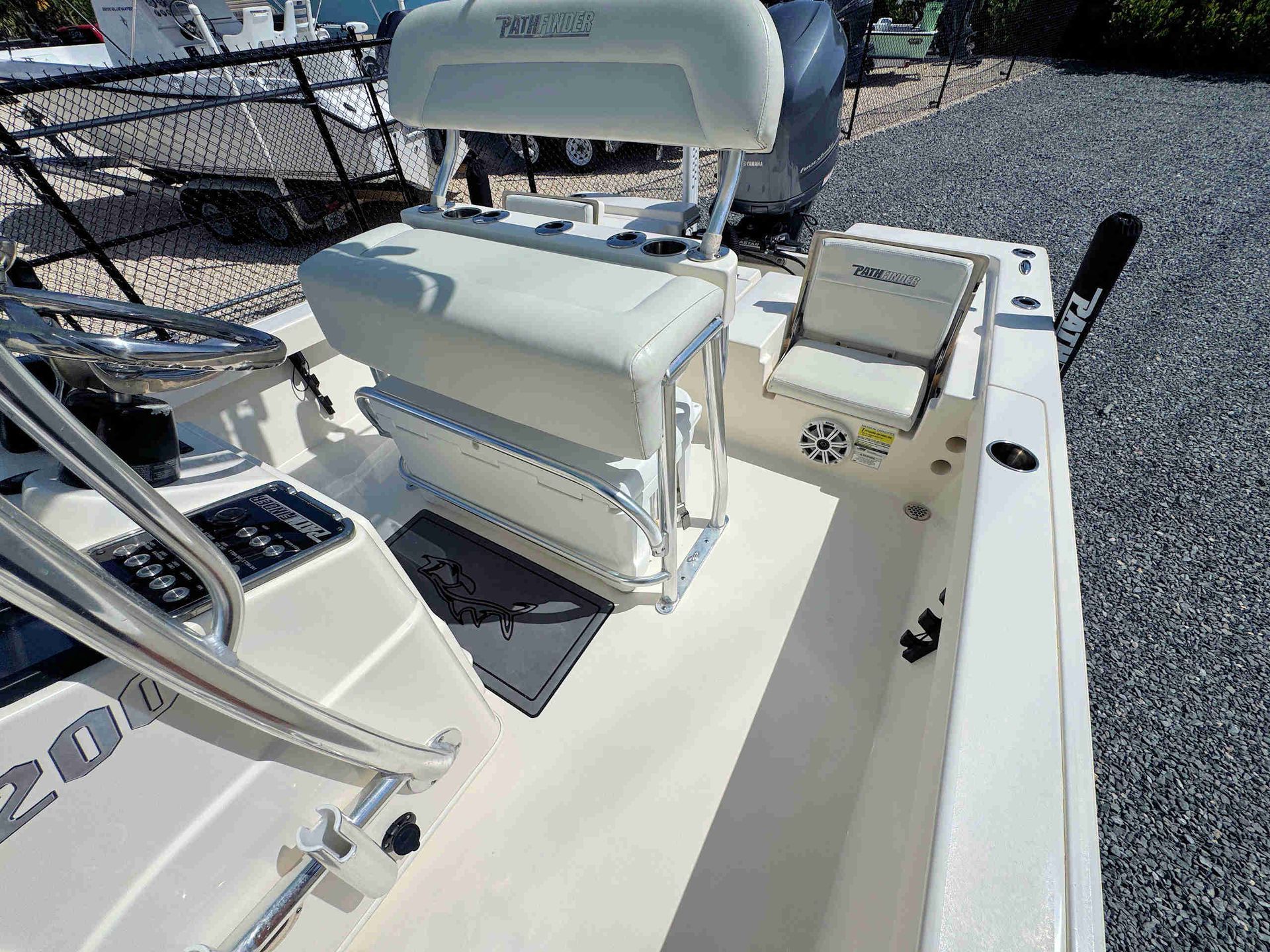 White boat cockpit with cushioned seats, steering console, and railings on a gravel lot