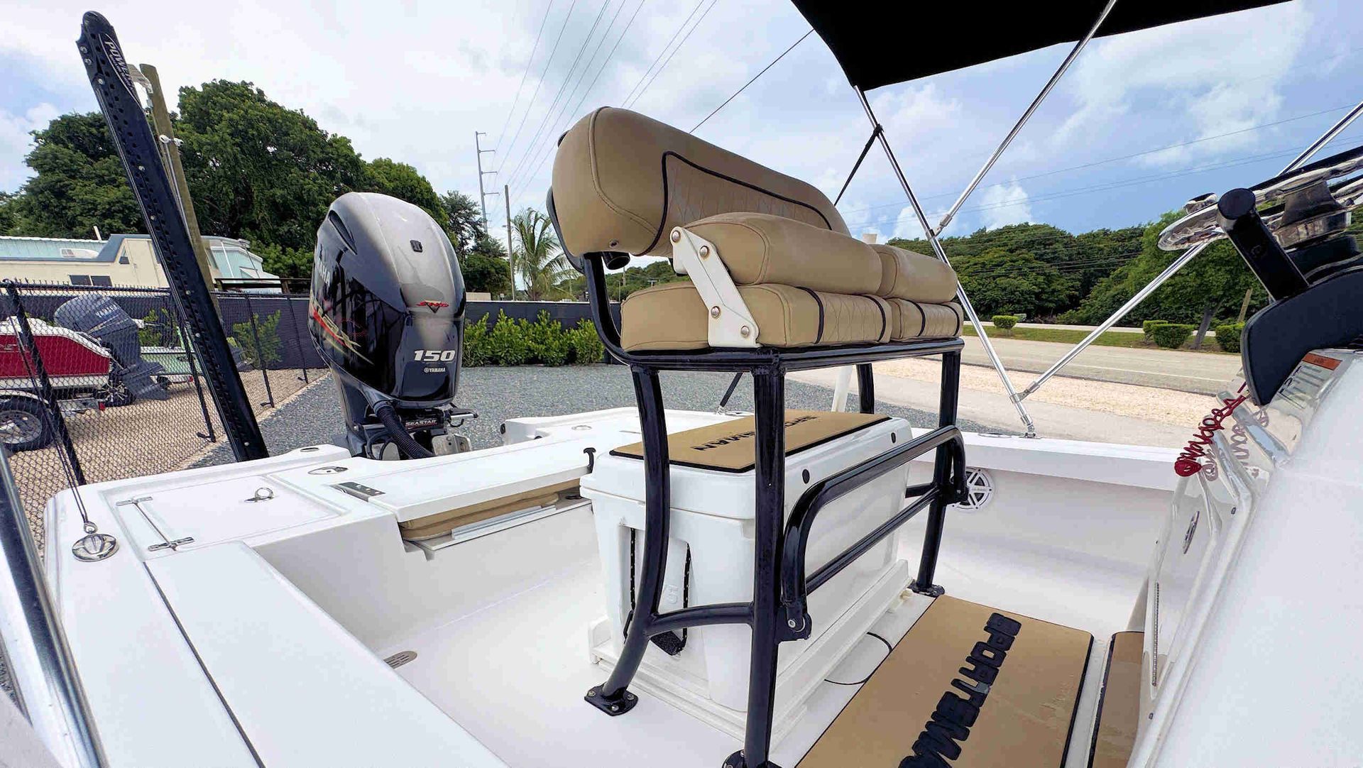 Boat deck with a mounted beige chair and outboard motor on calm water.