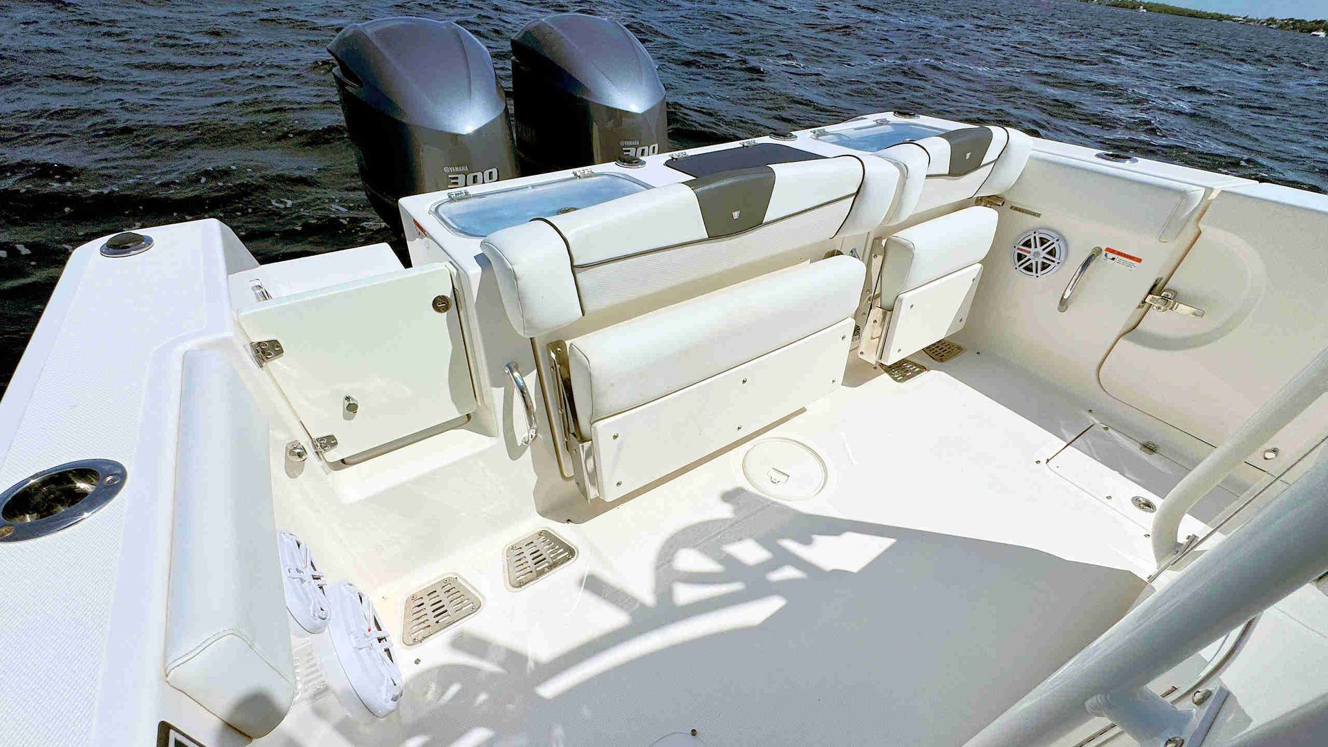 White boat deck with cushioned seating and twin outboard motors on the water