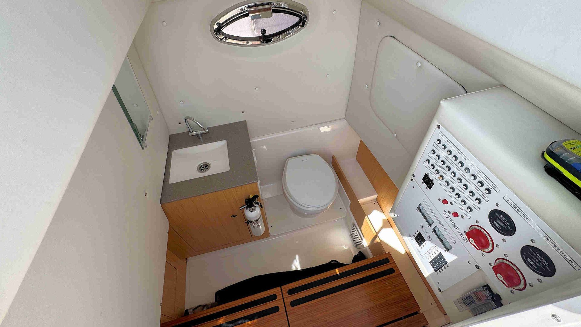 Center-console bathroom with toilet, sink, and control panel, viewed from the doorway.