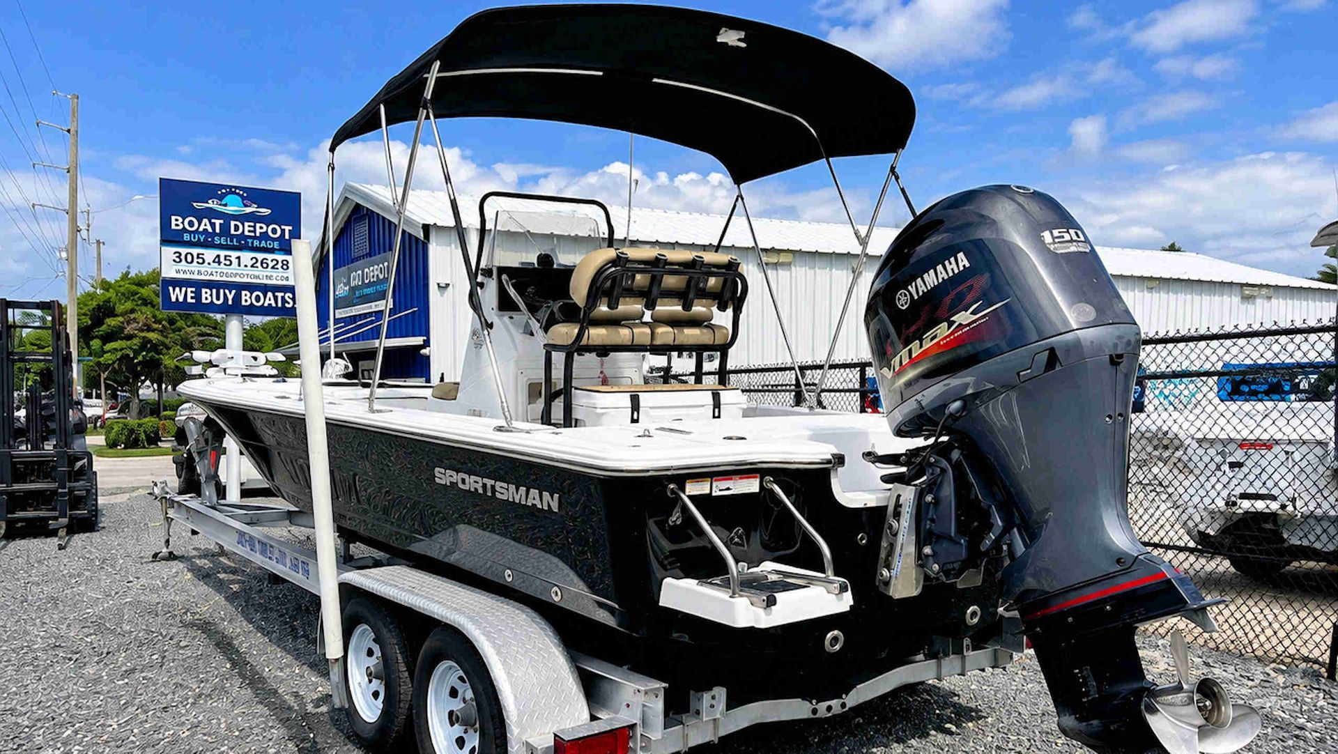 Black fishing boat on trailer with black bimini top and outboard motor in a marina lot