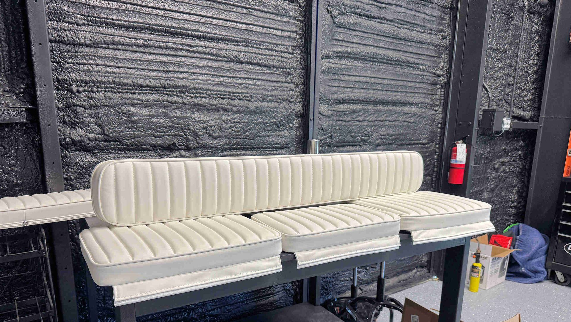 White upholstered sectional bench with tufted backrest in a workshop-like room.