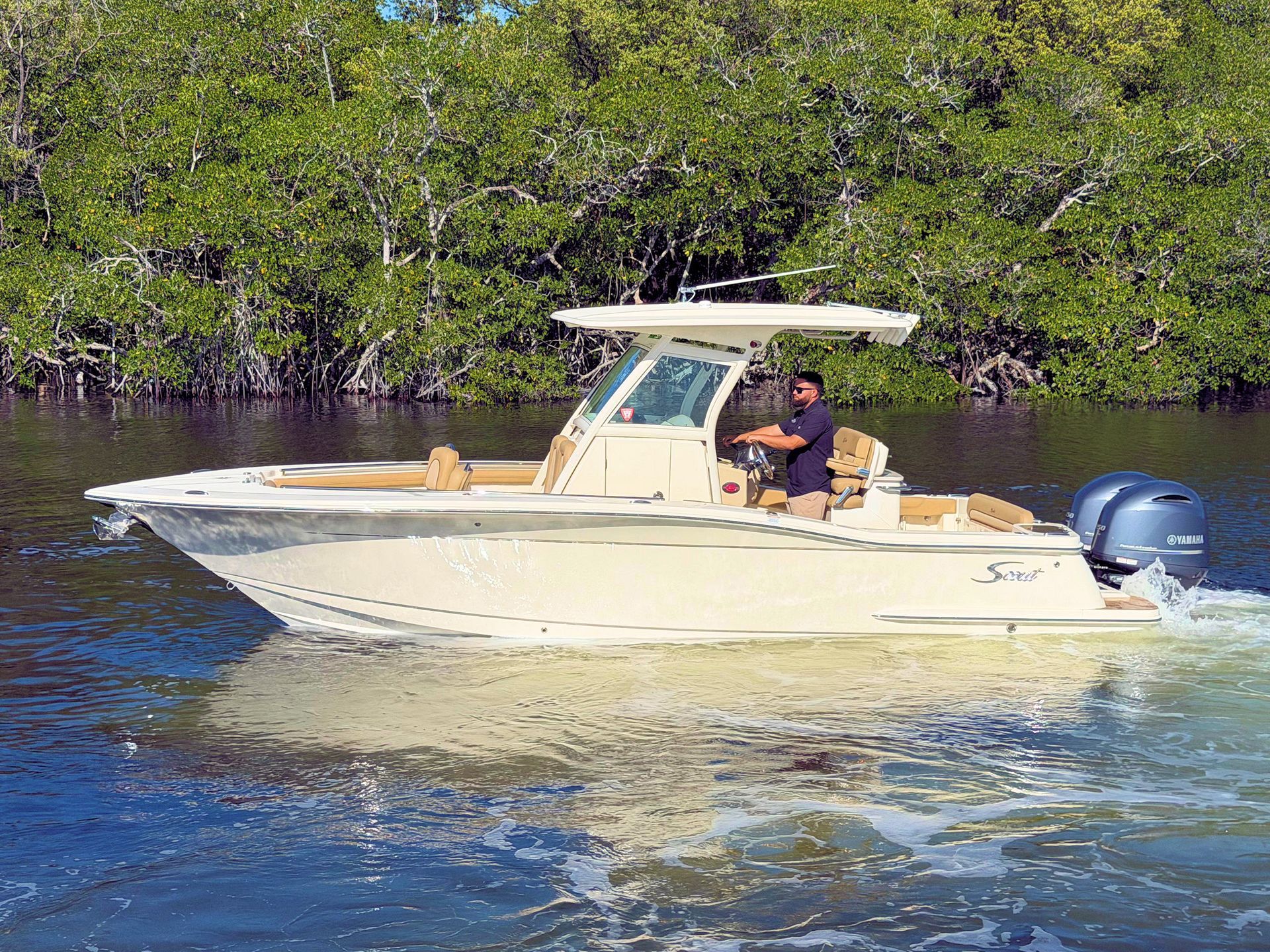 Small white center console boat cruising on calm water near mangrove shore, with a person at the helm
