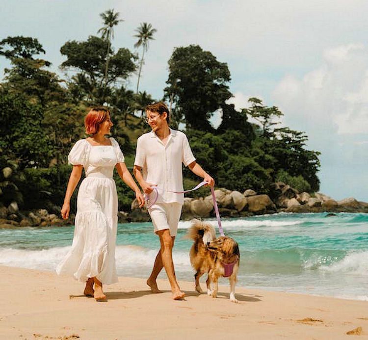Coupe walking on the beach with a dog on a leash.