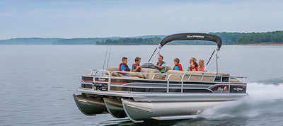 A pontoon boat with a group of people on a lake. They are wearing life vests.