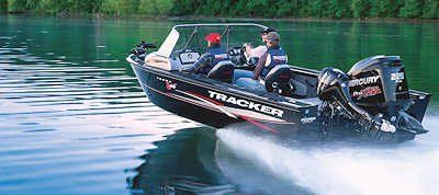 A black Tracker boat speeds across the water, two people are onboard.