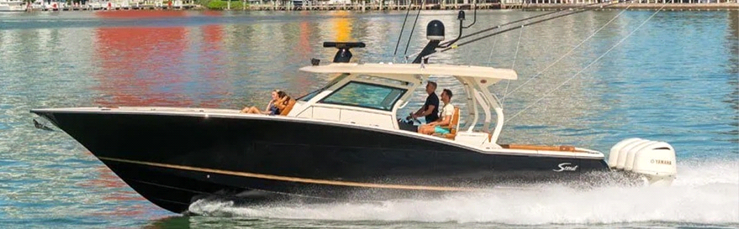 Black center console boat cruising on calm water with two people aboard near a shoreline