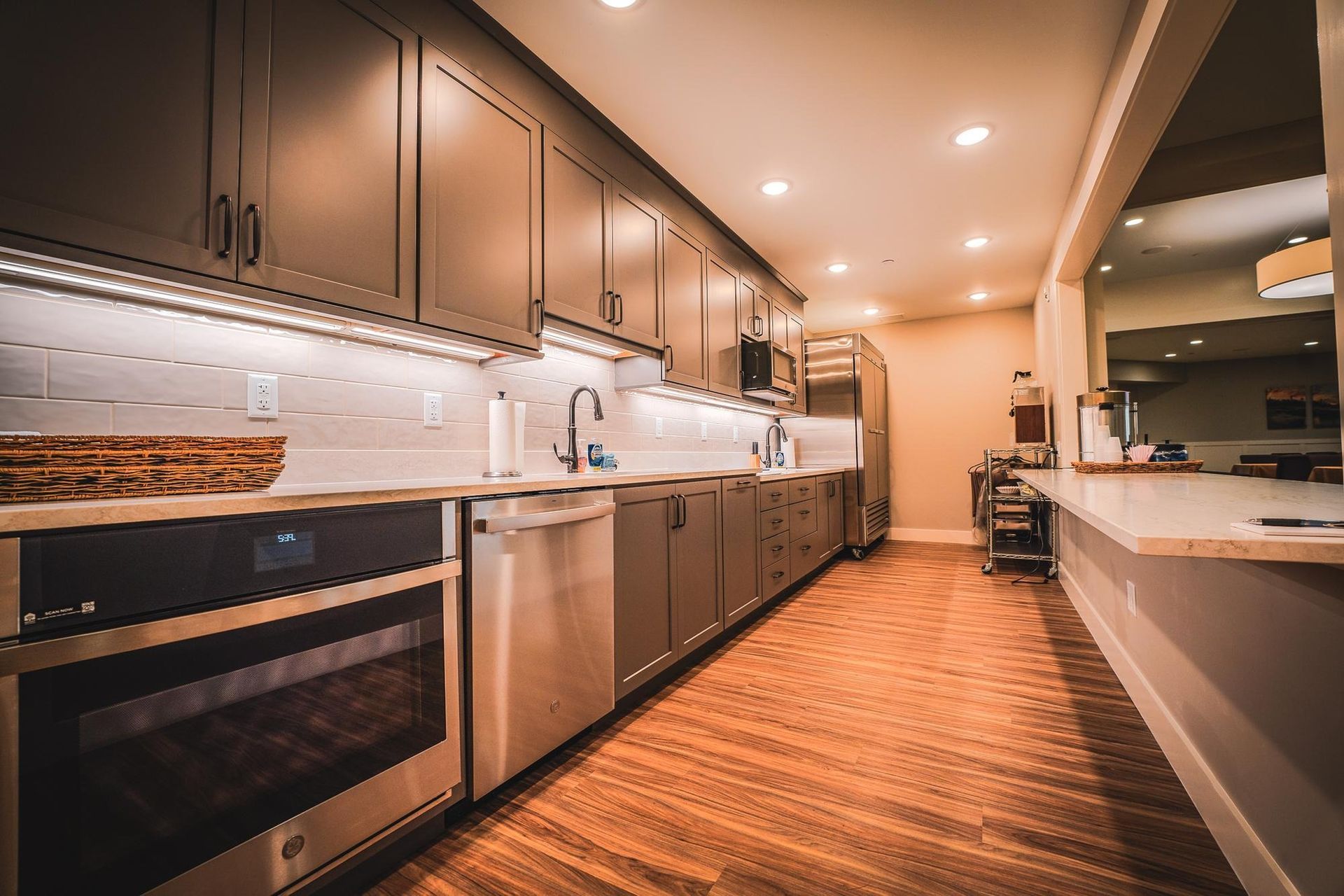 Modern kitchen with dark gray cabinets, stainless steel appliances, and wood flooring.